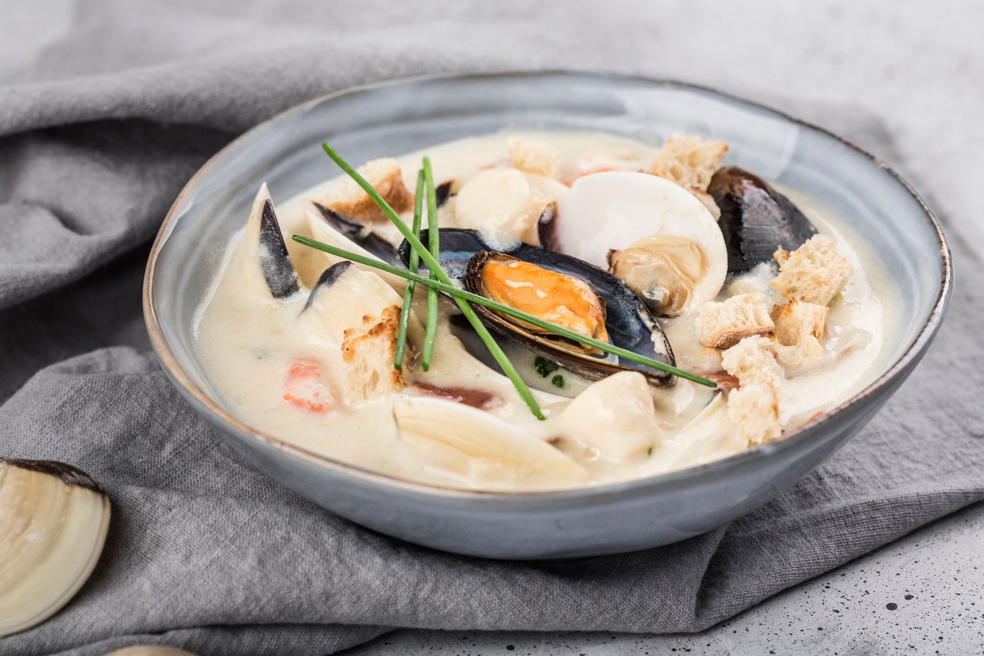 Seafood soup with mussels and herbs in a gray bowl on a cloth napkin