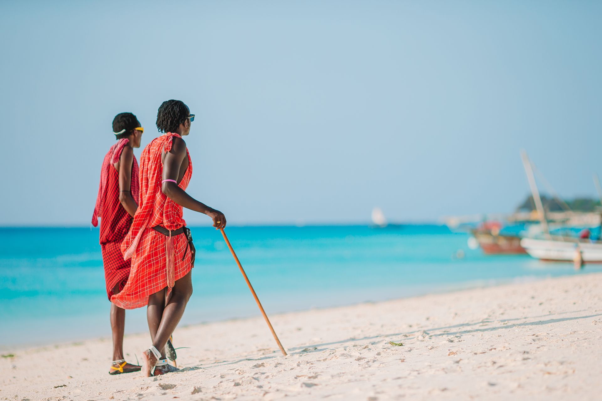 Two traditional Maasai warriors in traditional clothing walking along Zanzibar beach 