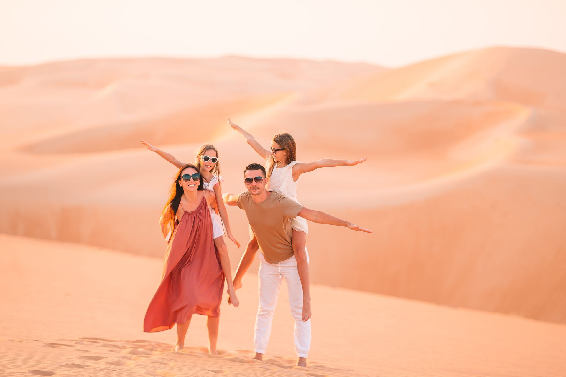 Family posing with arms outstretched on desert sand dunes at sunset