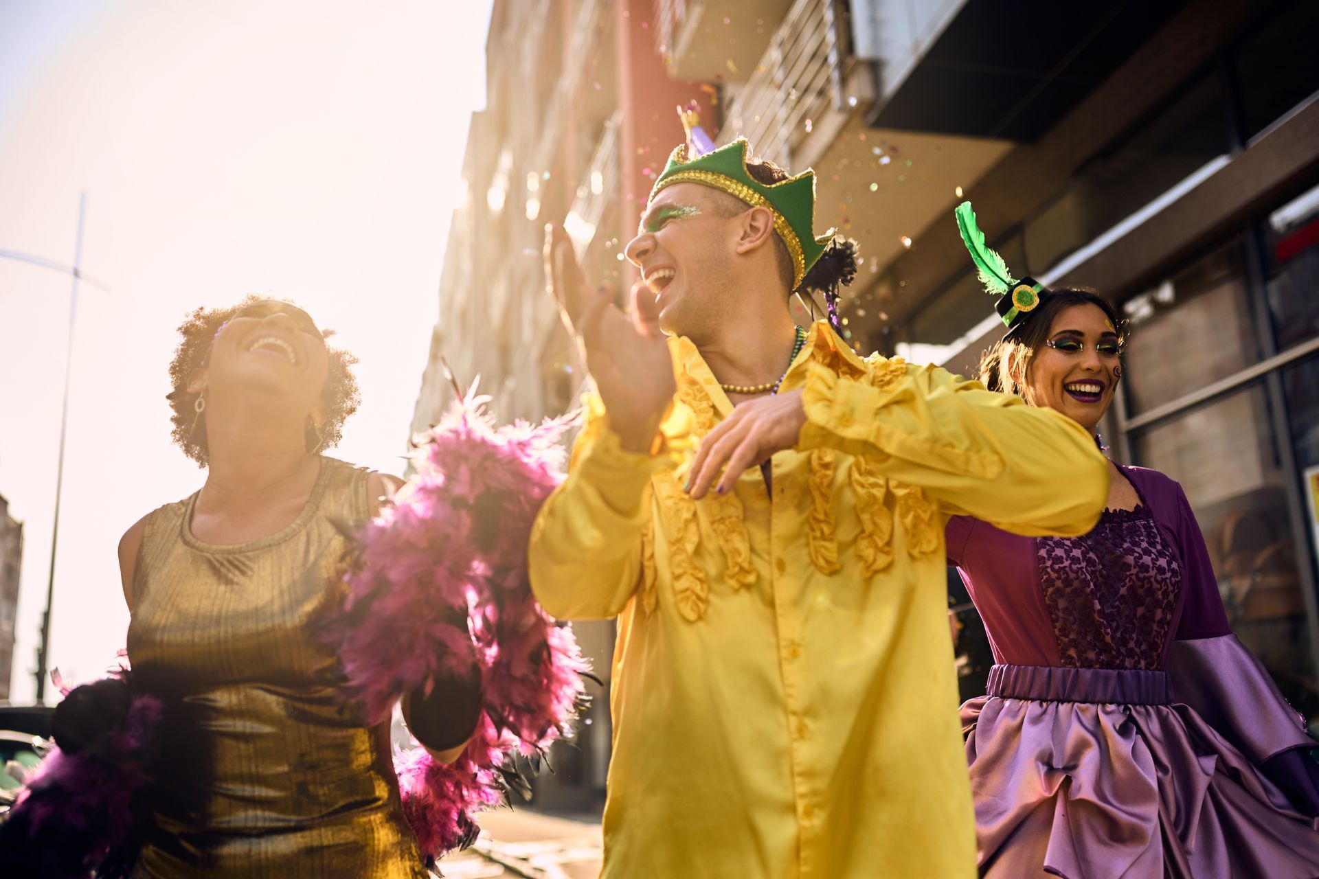 Three people dancing in colorful costumes on a city street during a lively celebration