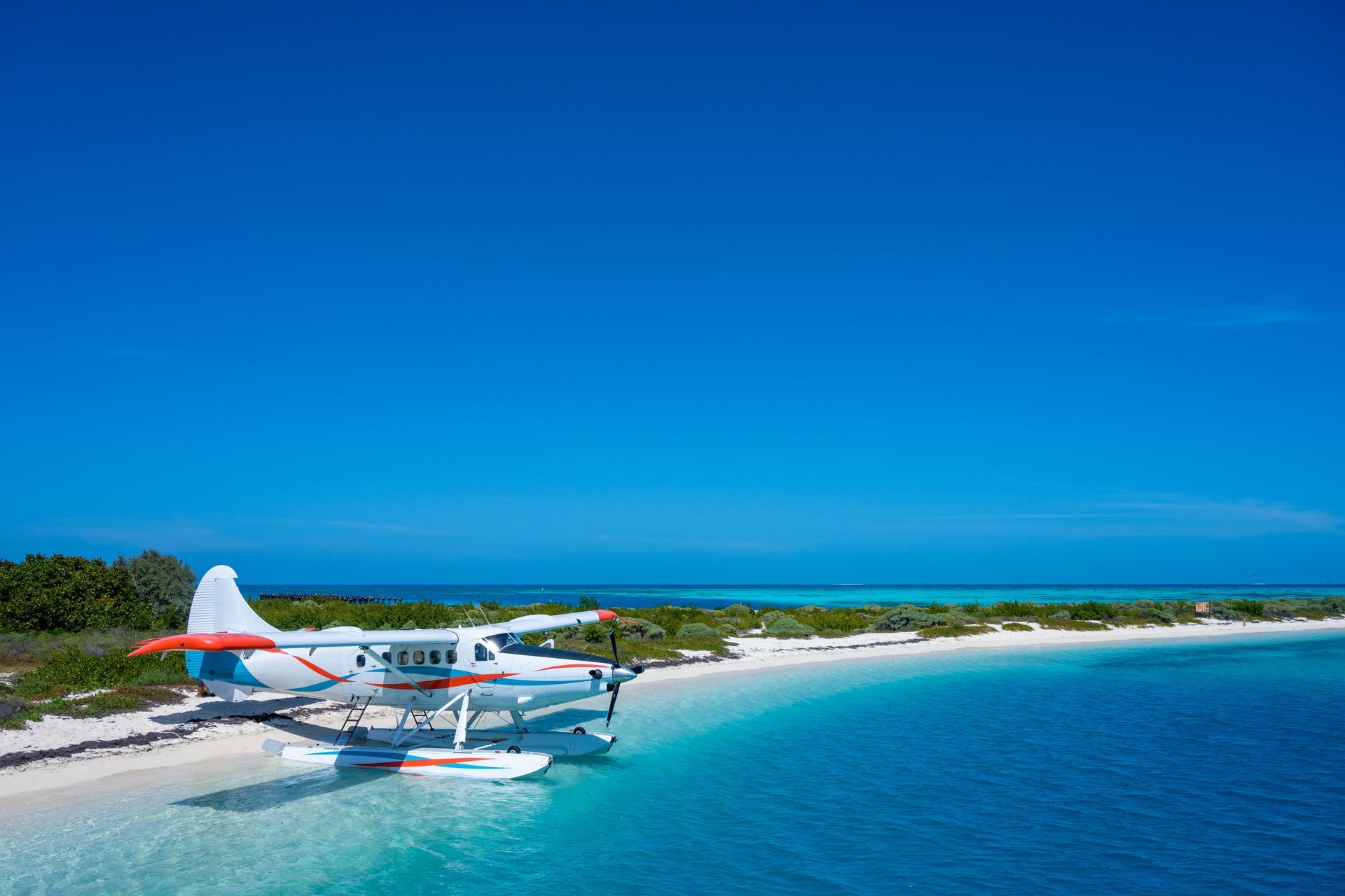 Seaplane floating by a white sand beach with turquoise water under a clear blue sky