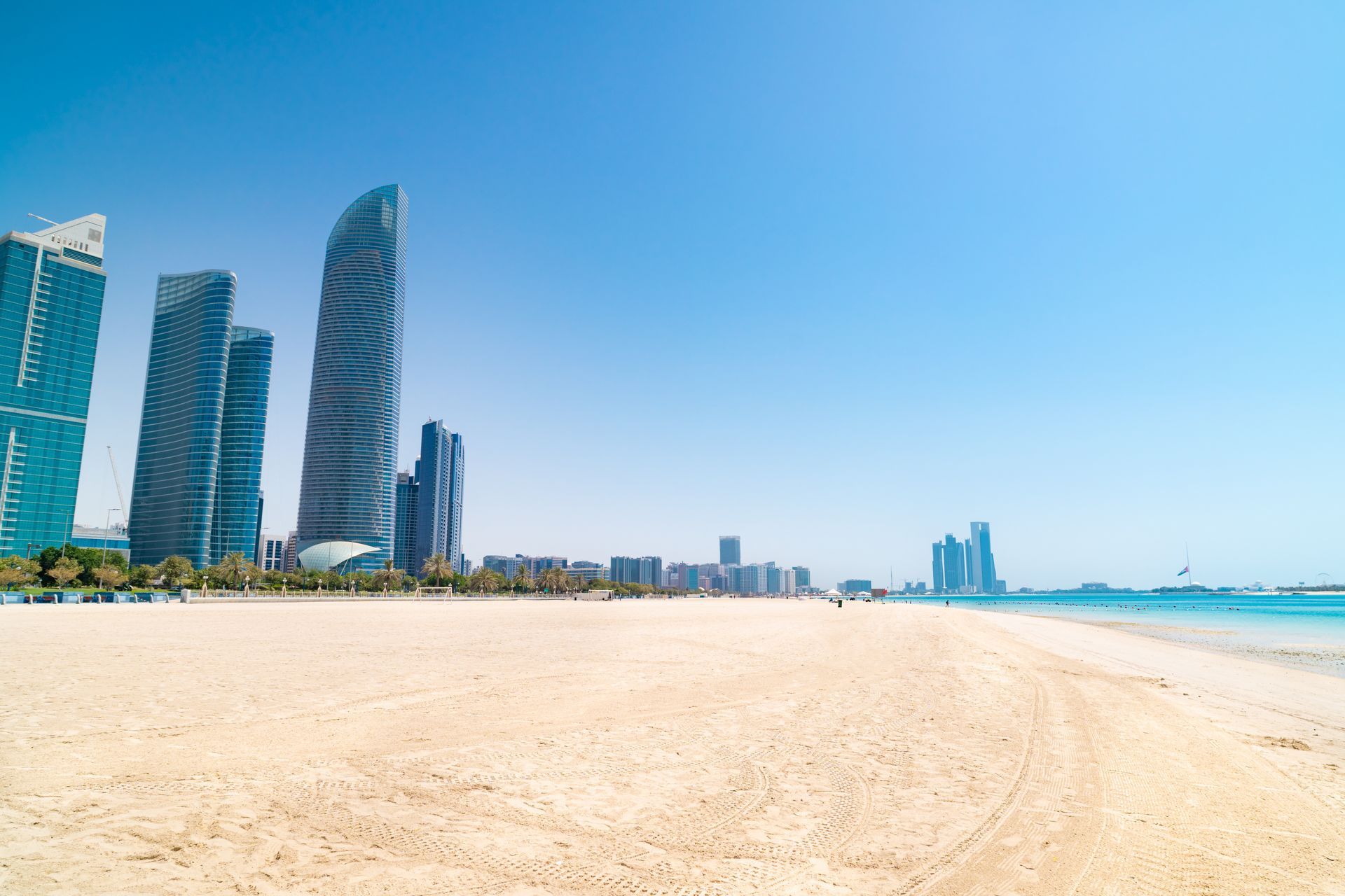 Wide sandy beach beside modern high-rise towers under a clear blue sky
