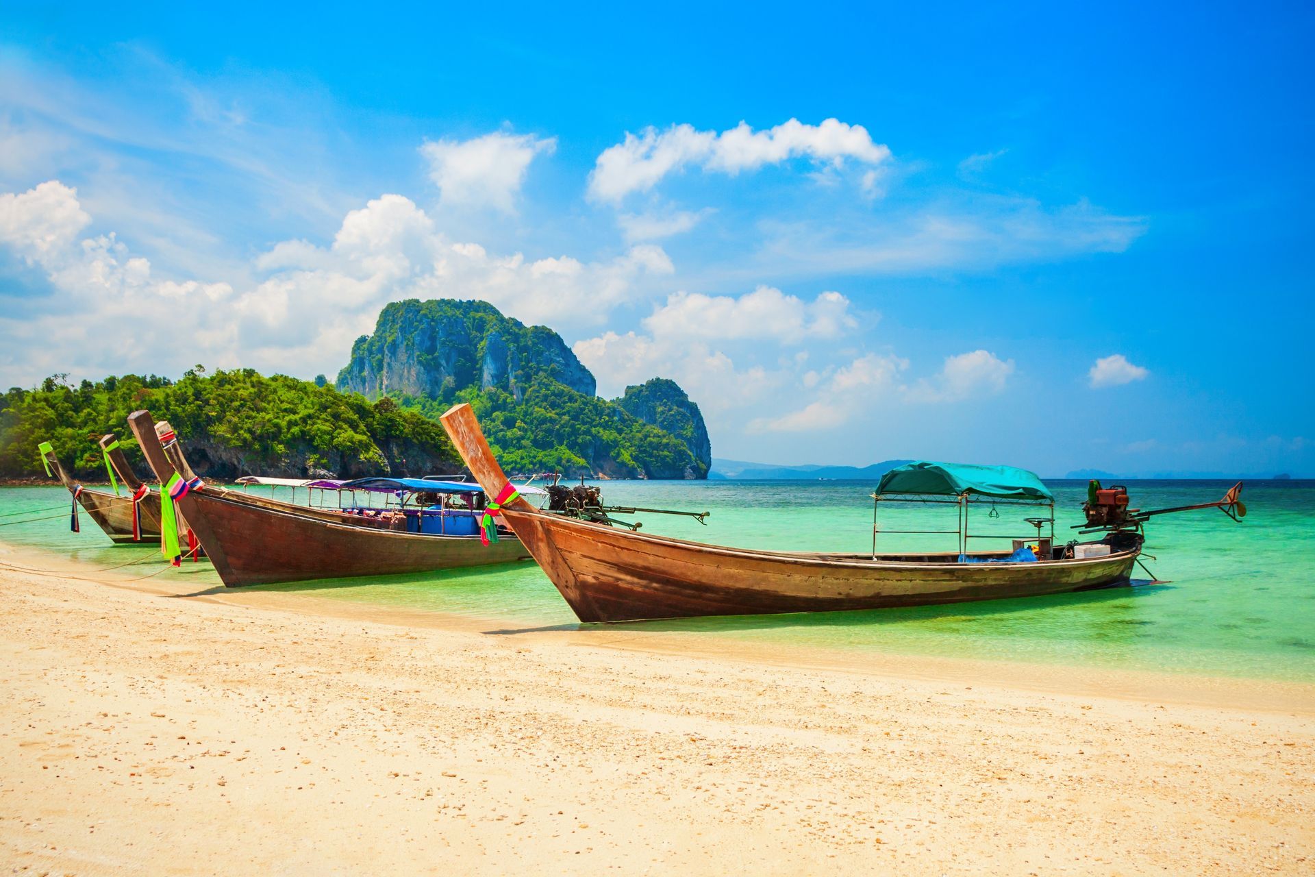 Long-tail boats on a tropical beach with turquoise water and limestone islands under a blue sky