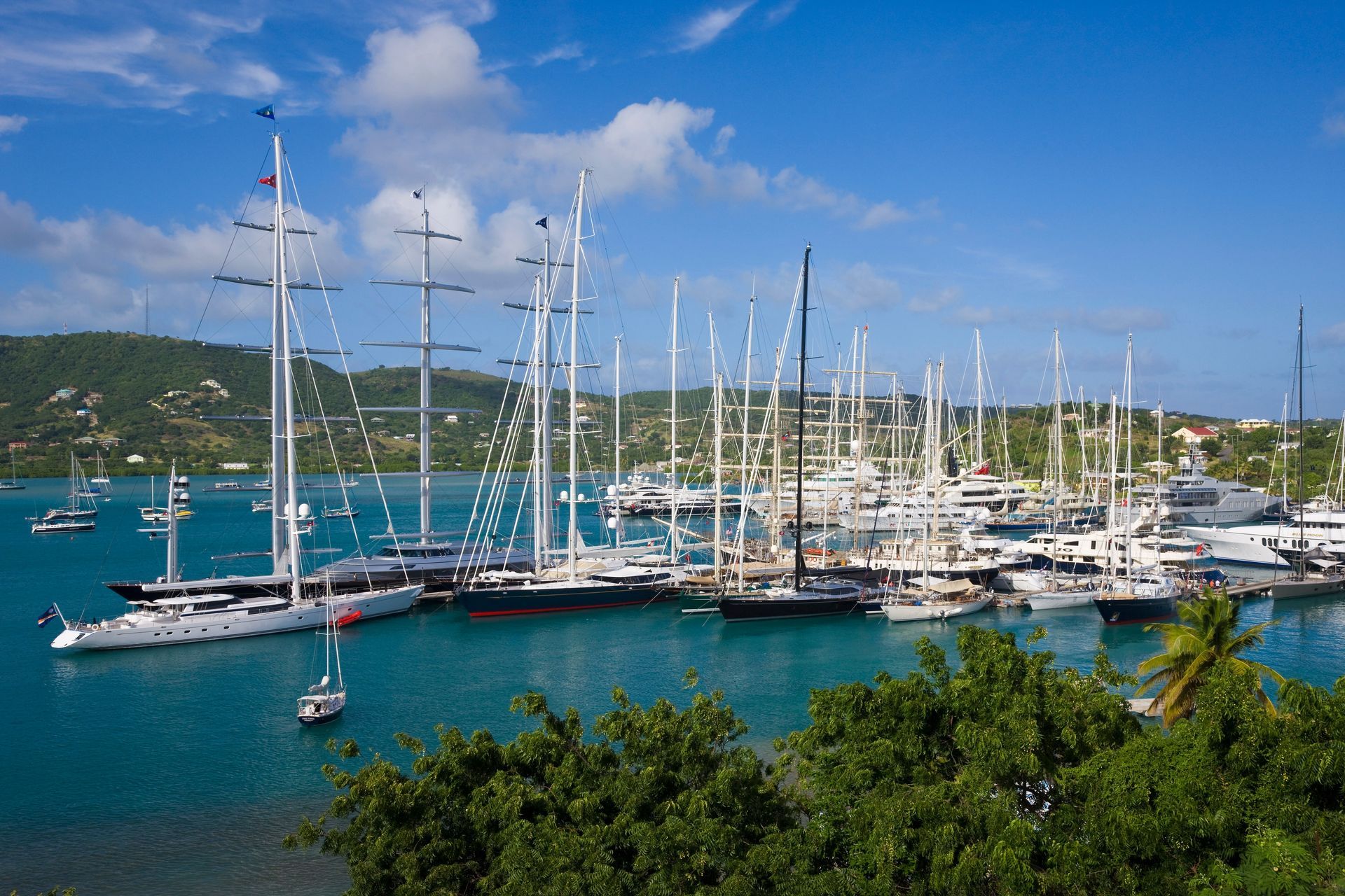 Yachts docked in a turquoise harbor with green hills and a blue sky