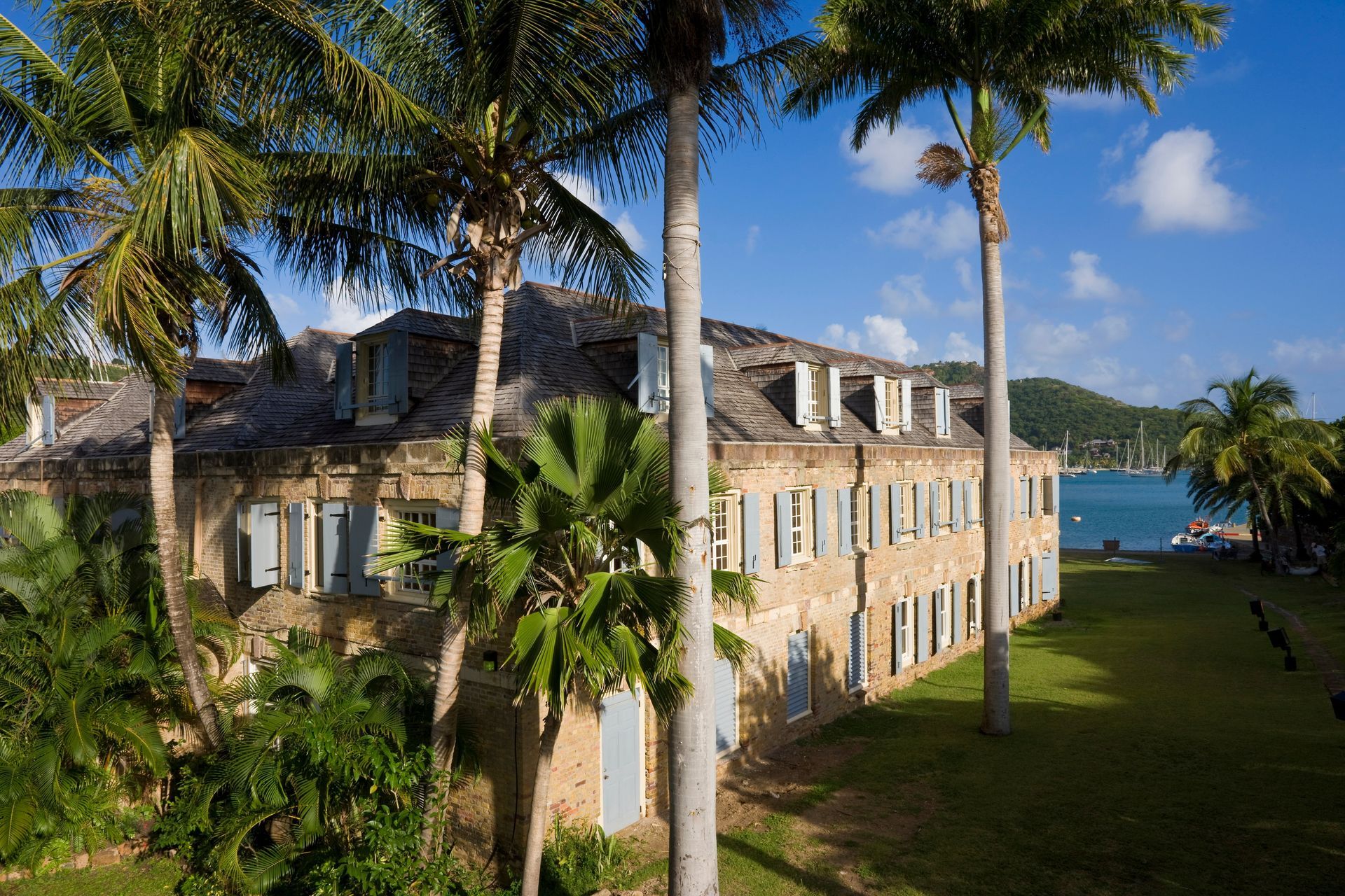 Historic beige building among palm trees by blue water under a sunny sky