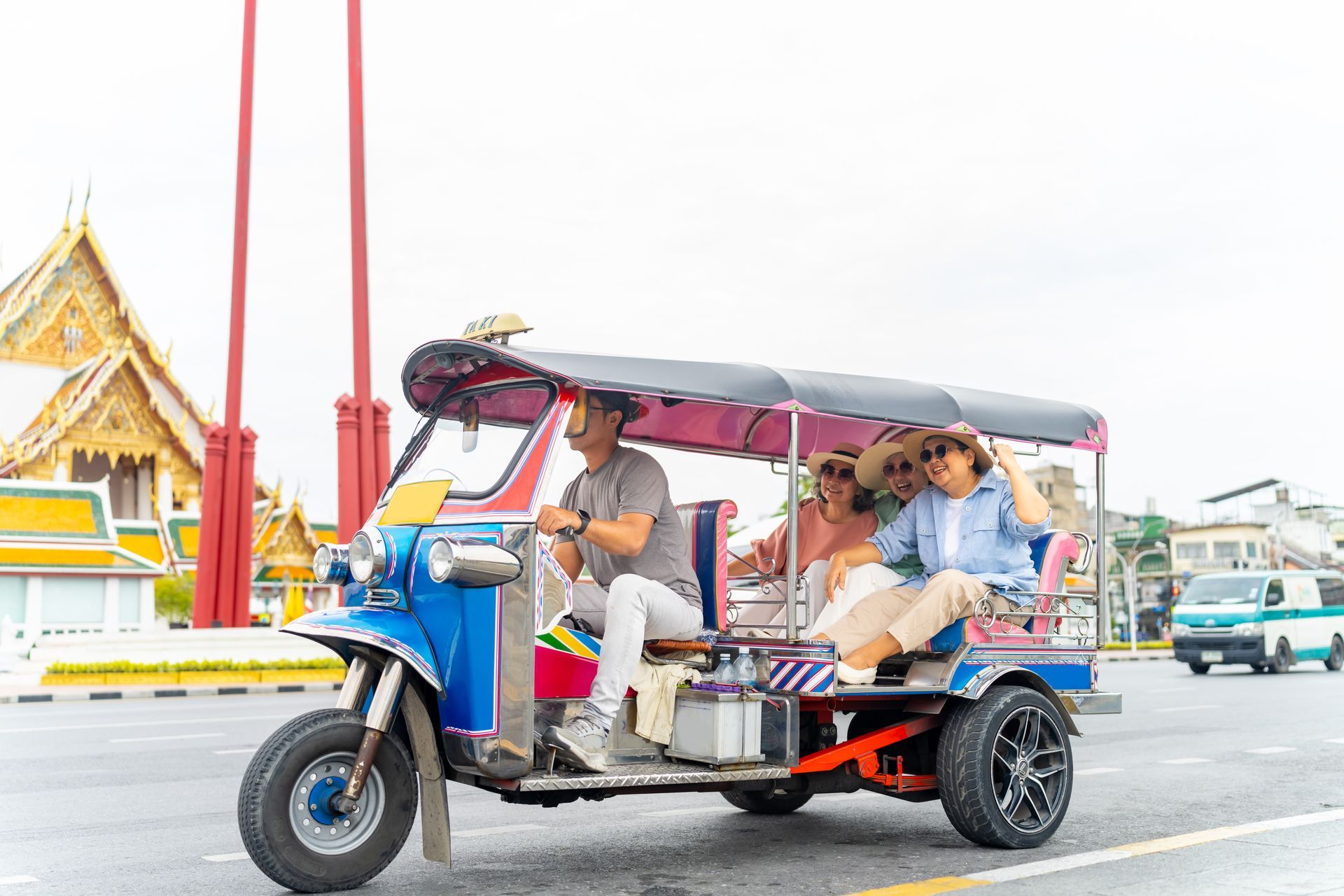 Tuk-tuk with passengers driving past a temple on a bright street