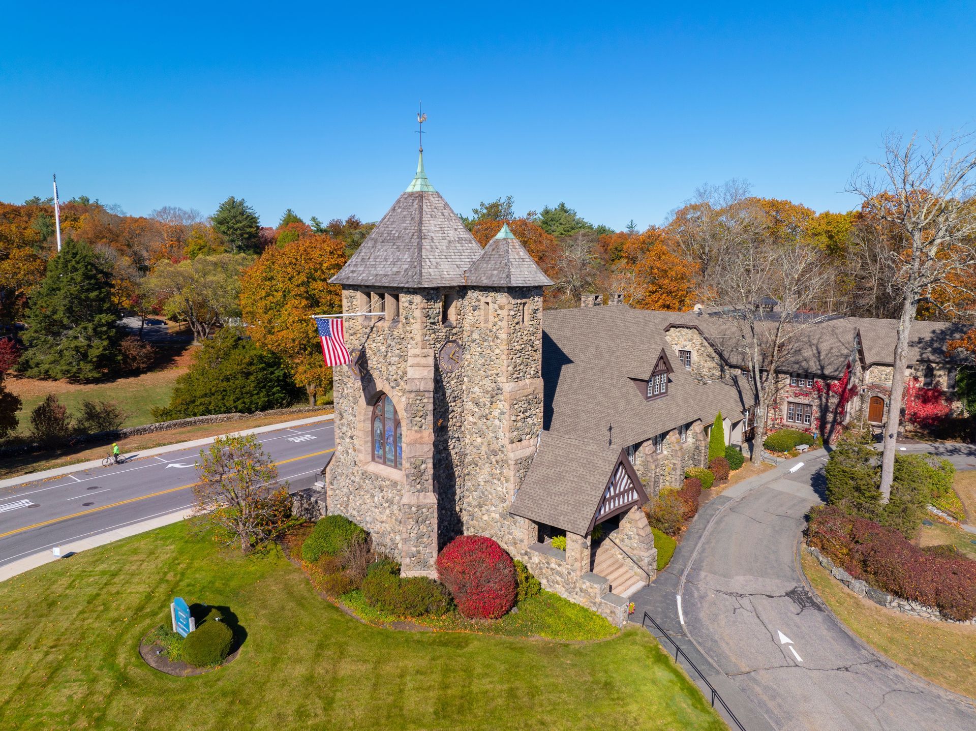 Stone church-like building with a tower beside a road, surrounded by autumn trees and grass.