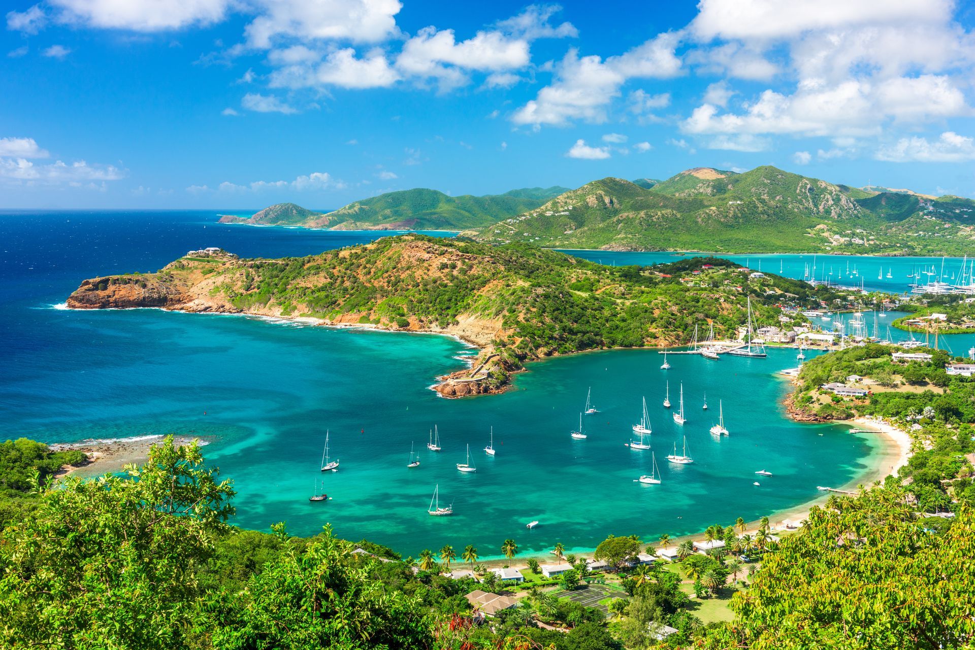 Tropical bay with turquoise water, sailboats, lush hills, and a bright blue sky