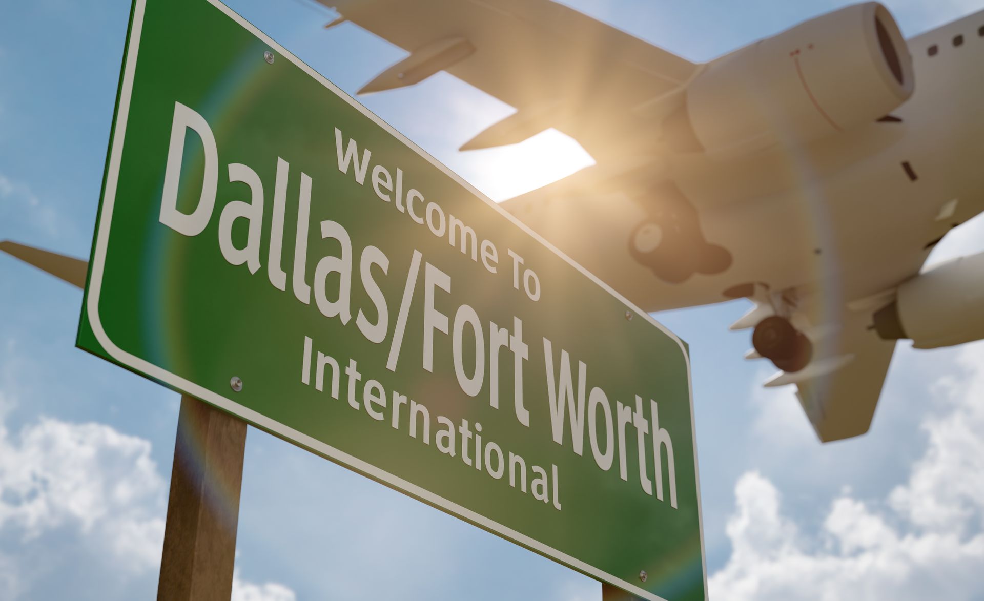 Green “Welcome to Dallas/Fort Worth International” sign with airplane overhead in bright sunlight