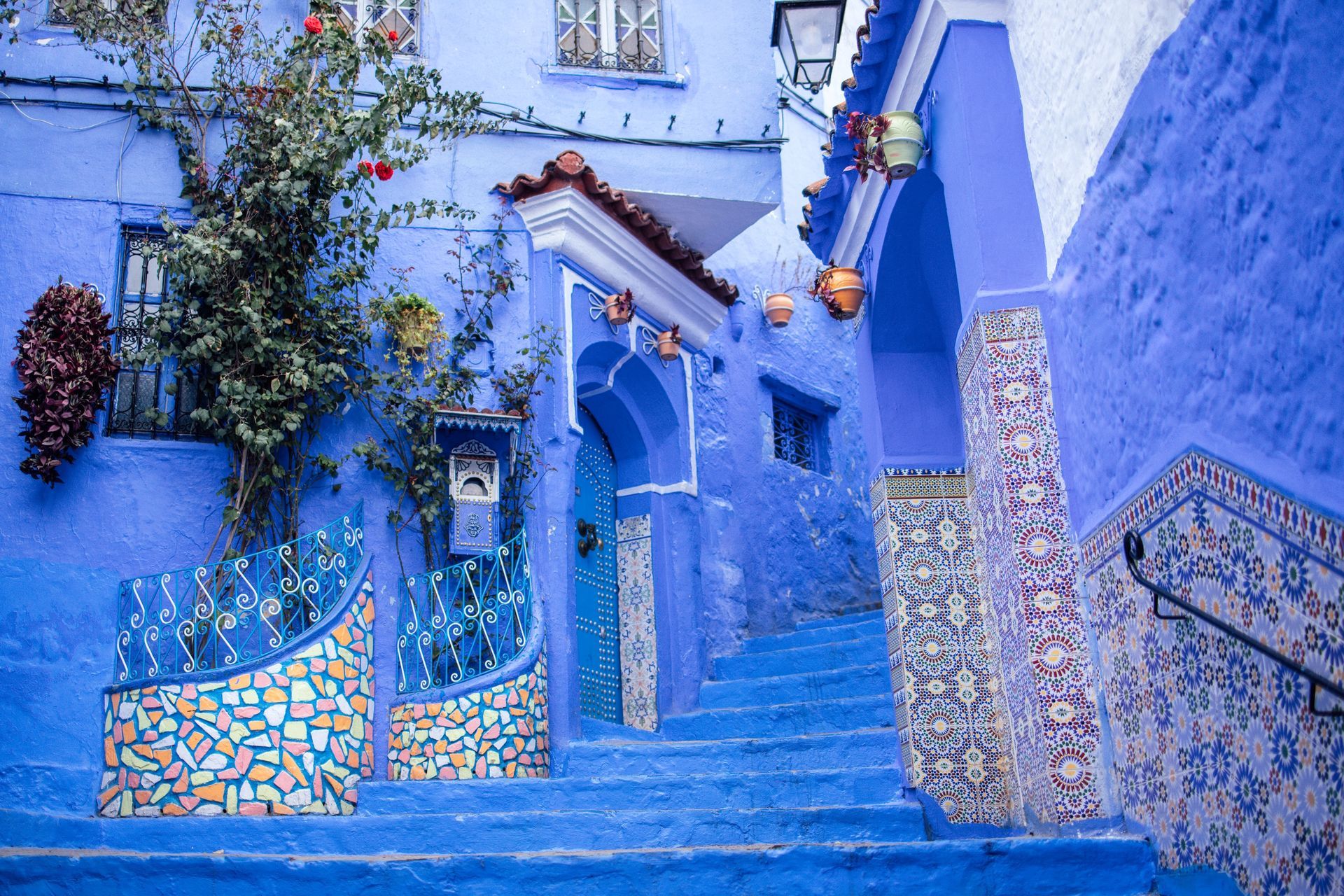 Blue-painted stairway and walls with colorful mosaic tiles in a narrow outdoor alley.