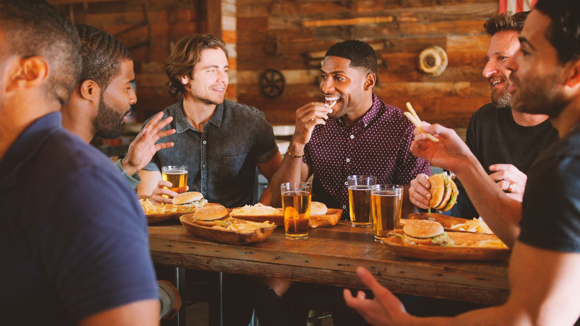People sharing drinks and conversation around a wooden table in a cozy bar setting
