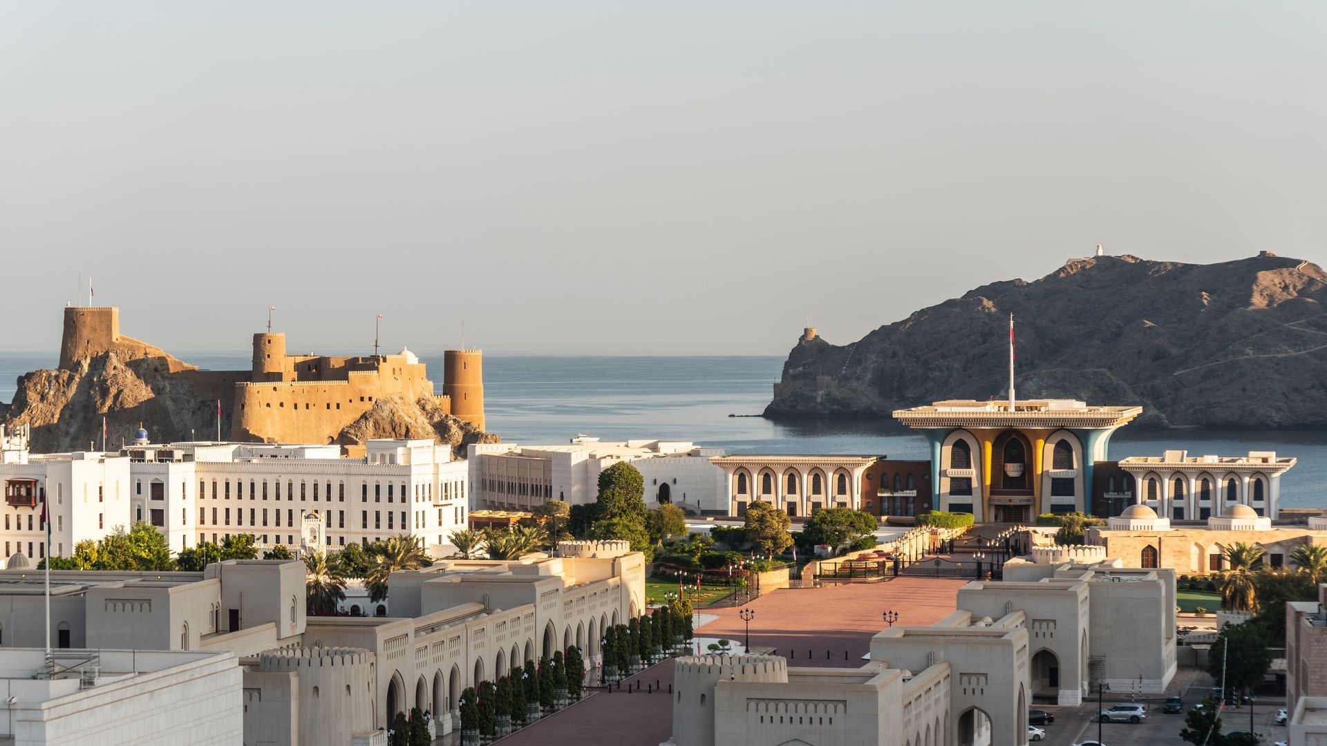 Coastal city skyline with white buildings, a seaside fort, and a bay at sunset