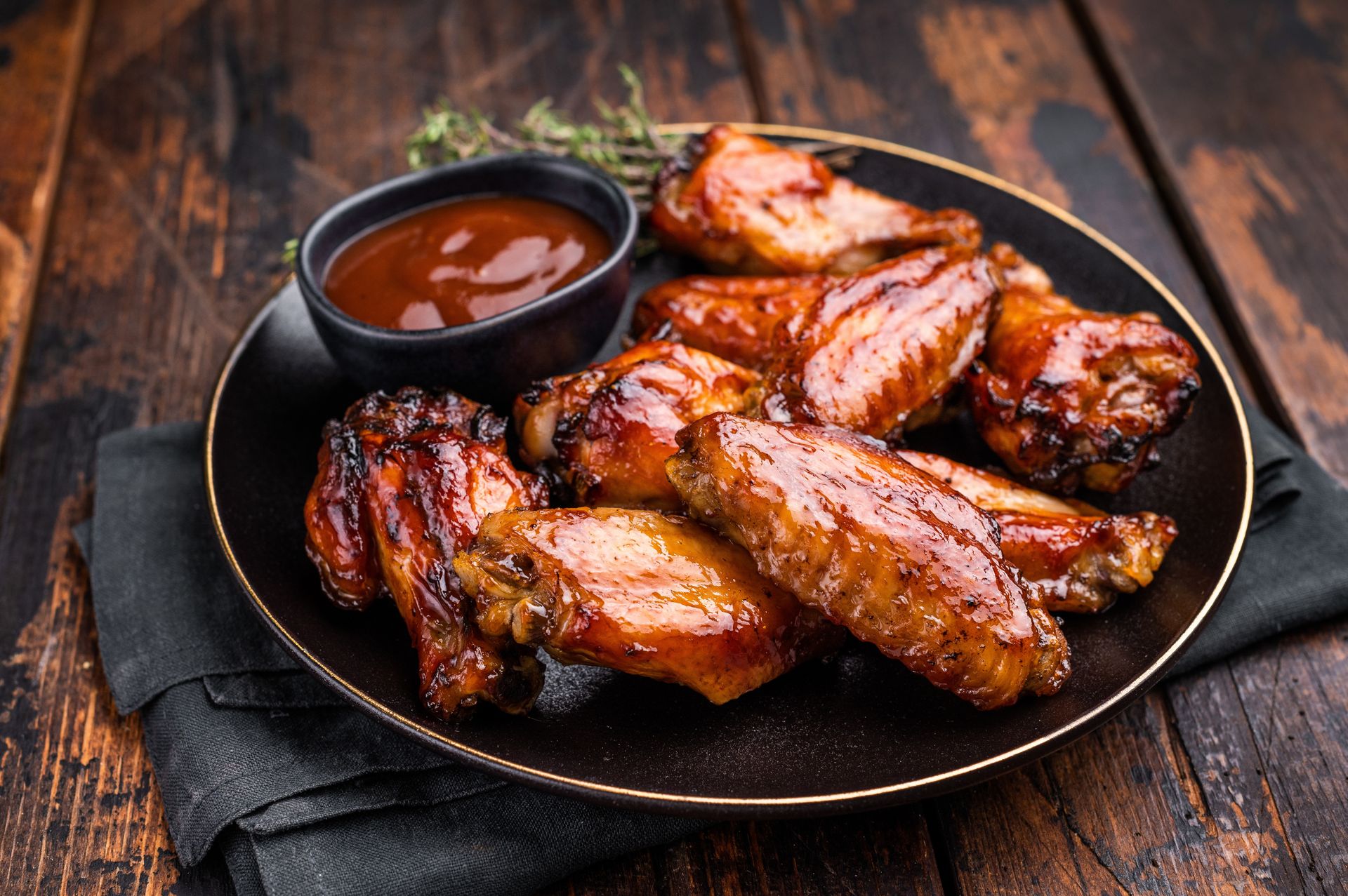 Barbecue chicken wings on a black plate with dipping sauce on a rustic wooden table