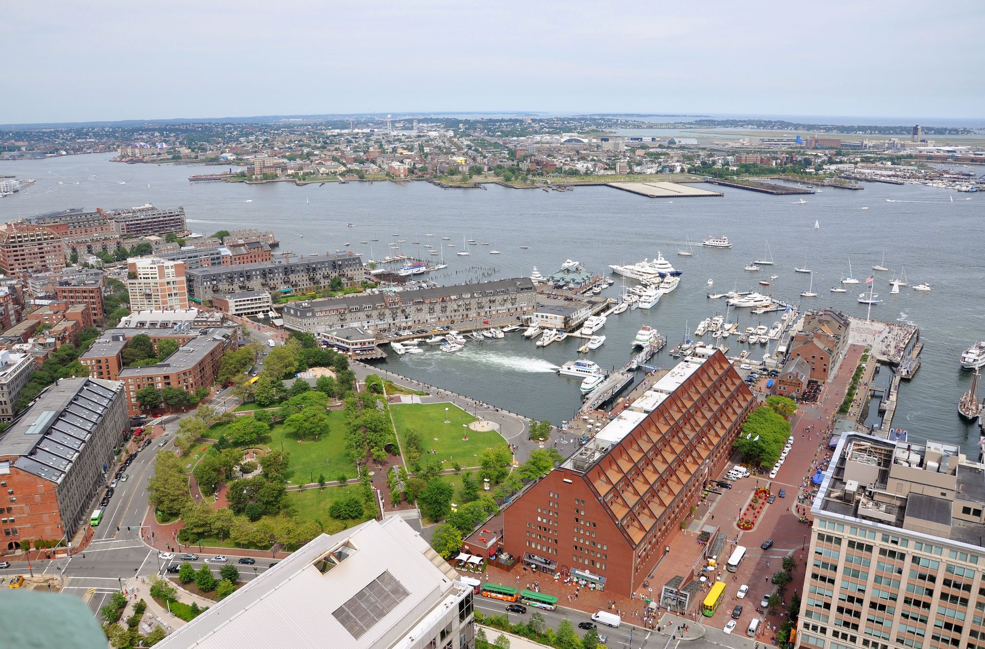 Aerial view of a marina and waterfront city with boats, red-brick buildings, and a broad bay.