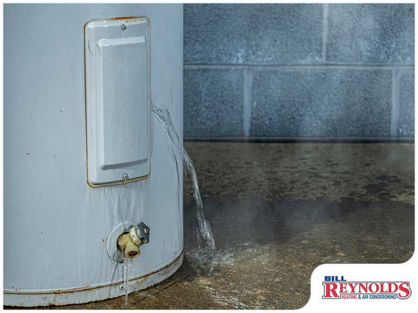 Water heater leaking water onto a concrete floor near a cinder block wall.