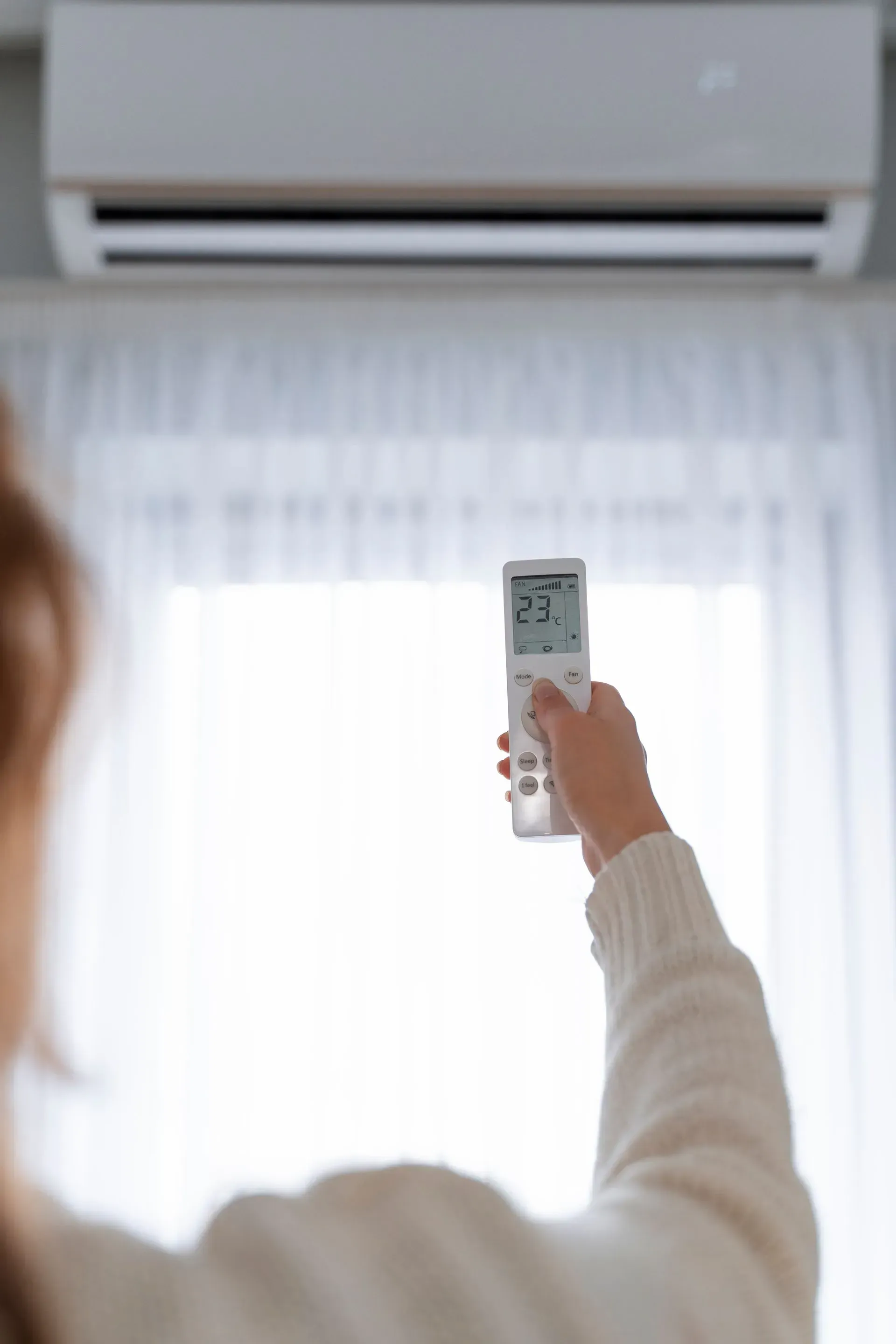 Person holding a remote, adjusting the temperature of a wall-mounted air conditioner, set at 23 degrees.