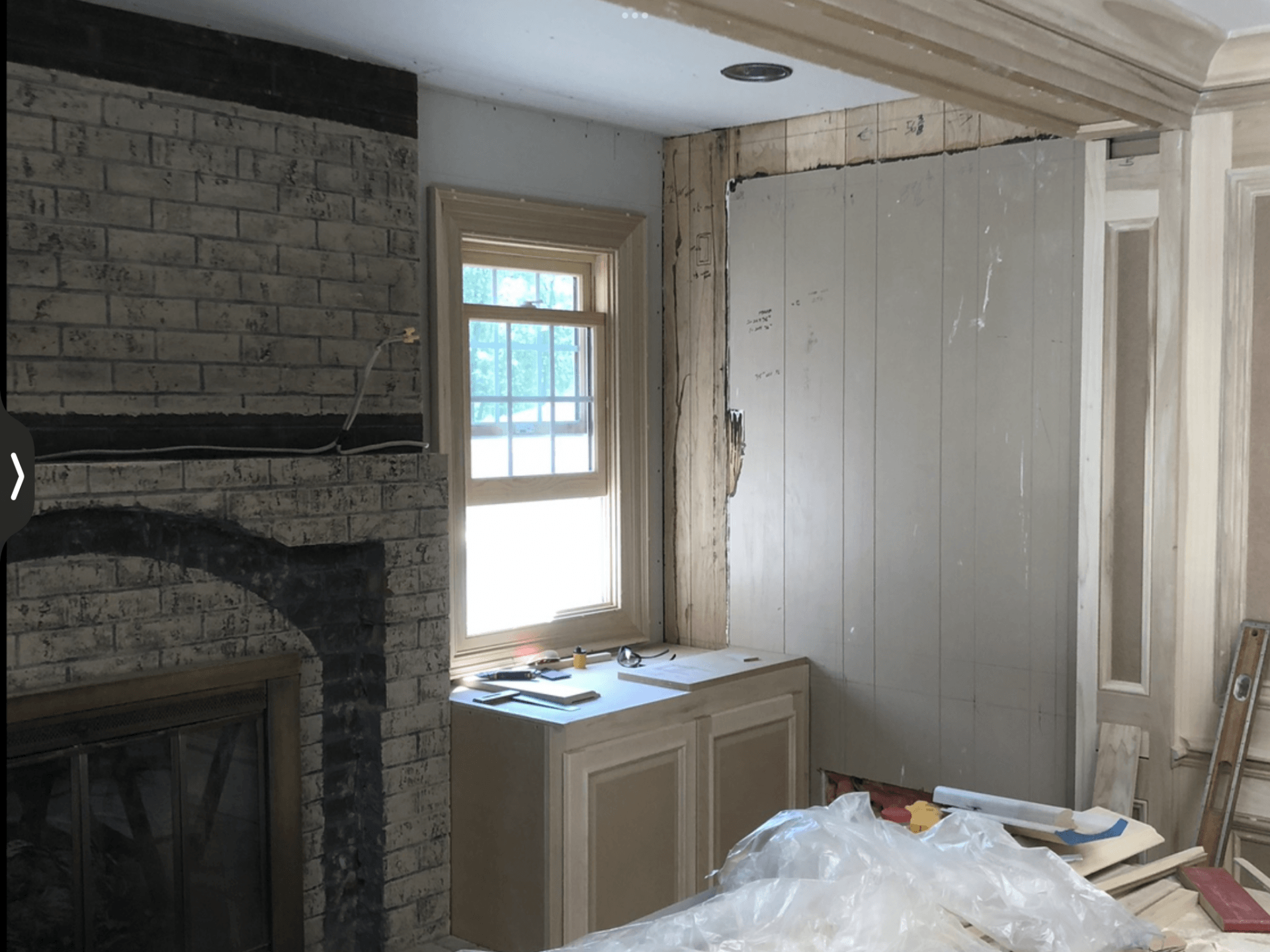 Interior view of a room under renovation. Brick fireplace, window, and wall paneling are visible.