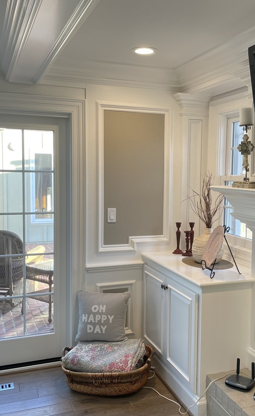 White-trimmed room corner with built-in cabinet and window. A door opens to a backyard; a throw pillow says 