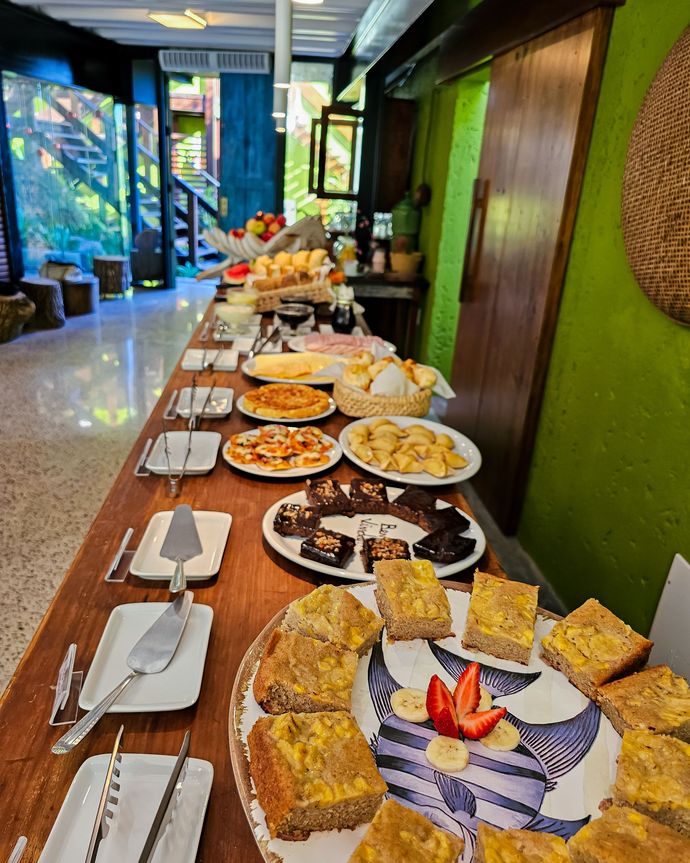 Mesa de buffet com pratos variados e sobremesas em uma área de jantar interna colorida.