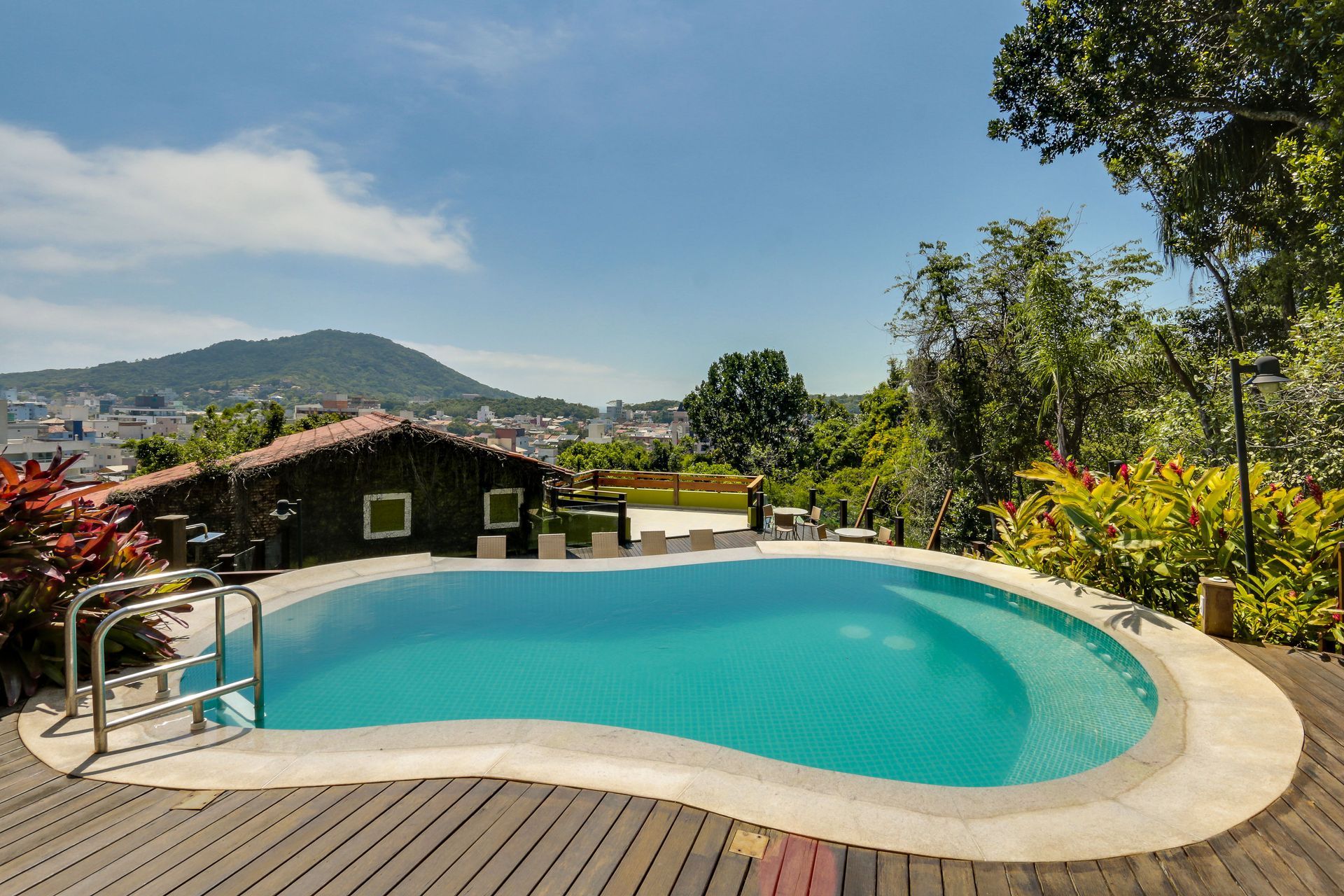 Piscina curva no quintal com água turquesa, espreguiçadeiras e vista para as montanhas sob um céu claro.