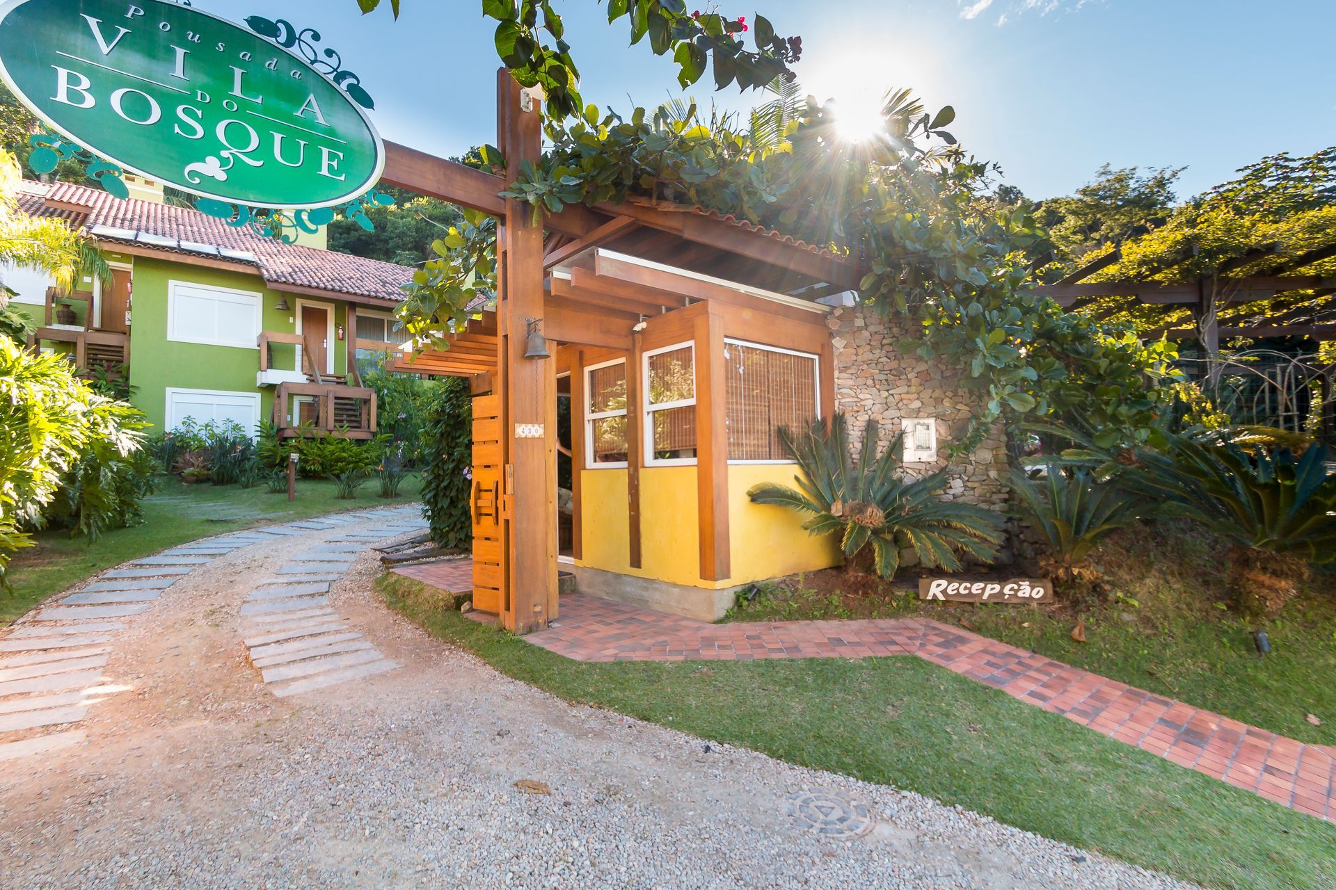 Entrada para um edifício rústico de tijolos e cor verde, com uma entrada de automóveis curva e caminhos de jardim exuberantes.
