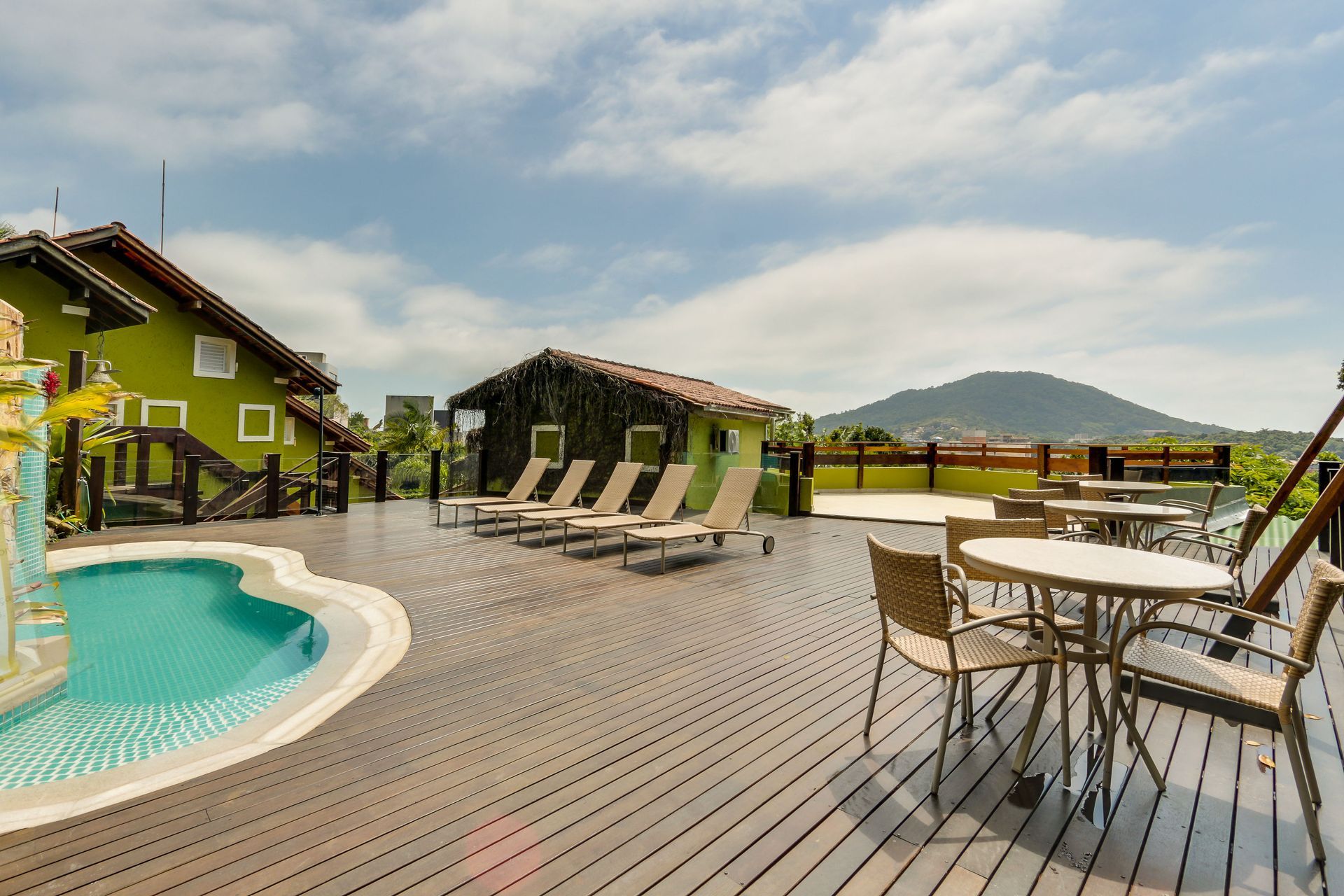Terraço da piscina do resort com espreguiçadeiras, mesas e vista para a montanha sob um céu parcialmente nublado.