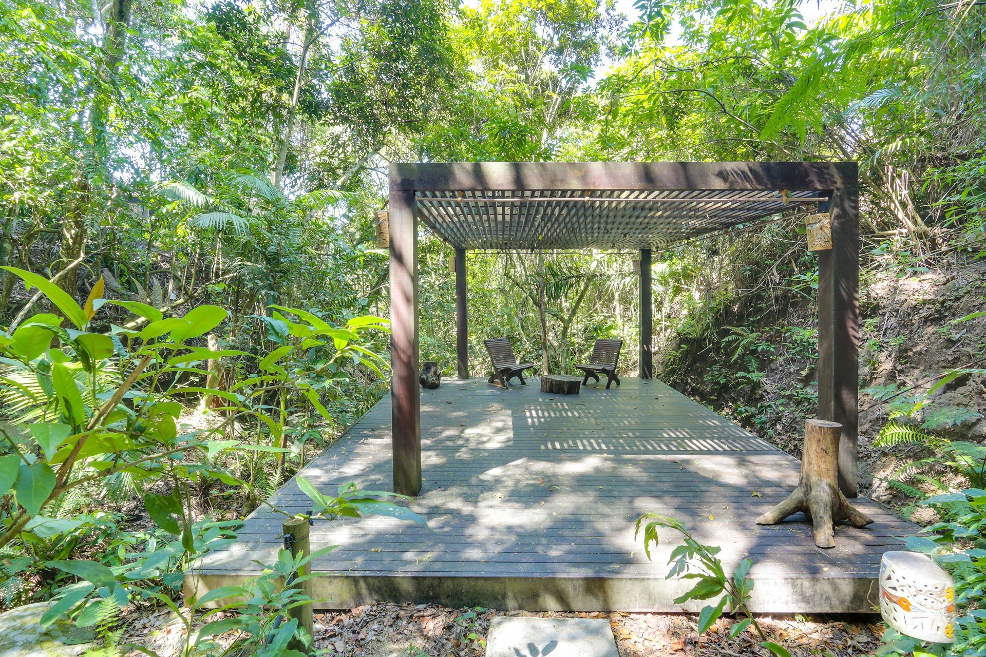 Gazebo de madeira sobre uma base de concreto em uma clareira verdejante na floresta.