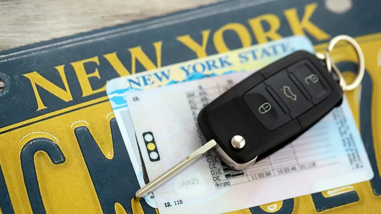 A car key fob rests on a New York State driver's license and new york plate