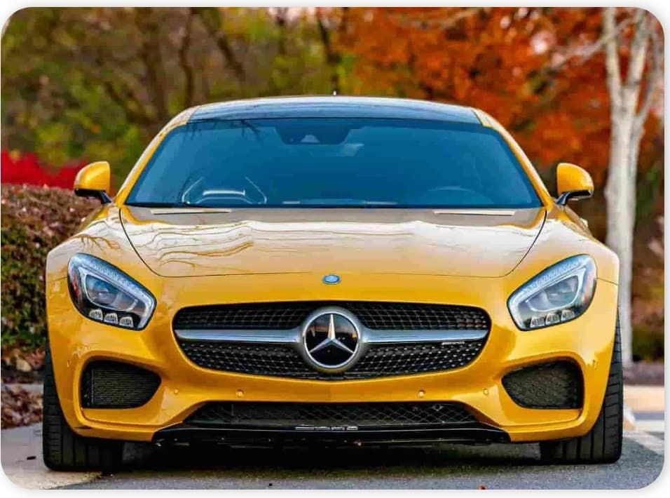 Yellow Mercedes sports car parked on a road beside autumn trees and bushes