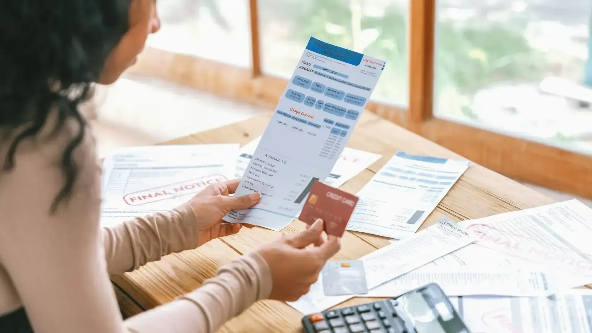 A person reviewing financial documents and a credit card at a wooden table.