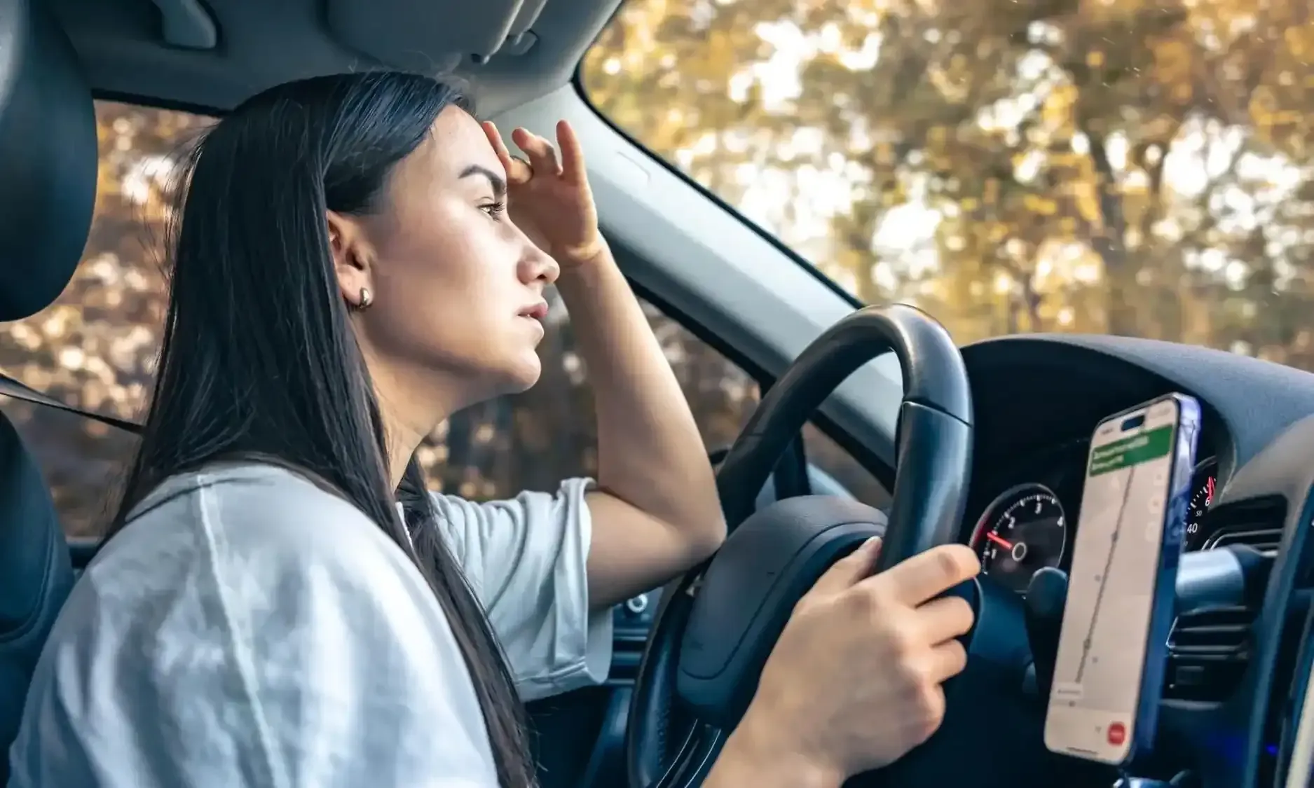 A driver looking out the window while holding the steering wheel, with a navigation app
