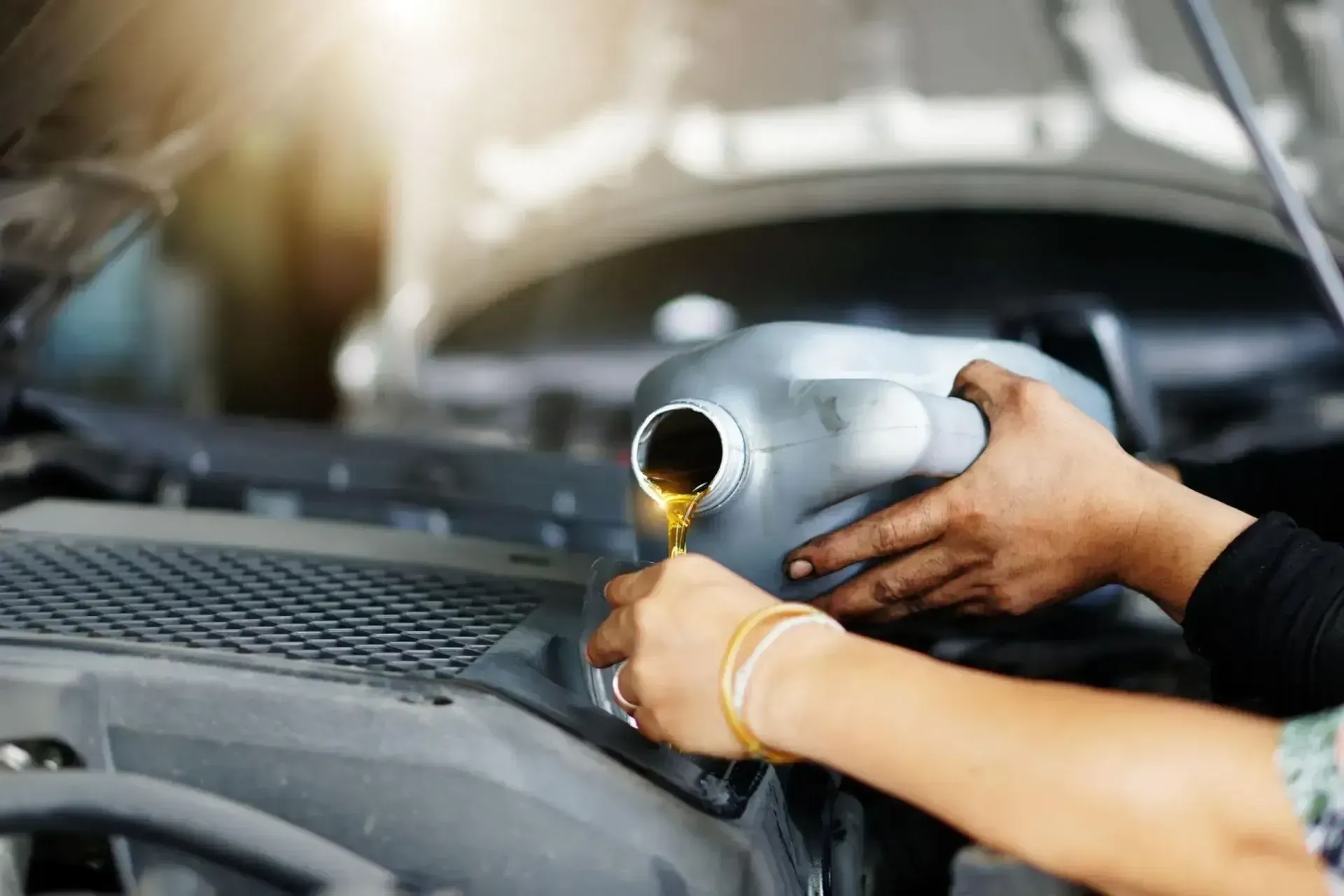 Hands pouring motor oil into an engine under the hood of a car.
