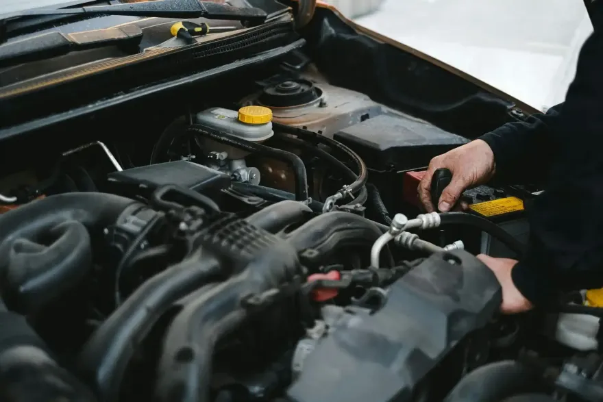 A mechanic works on a car engine, shown from a high-angle view as they reach into the hood
