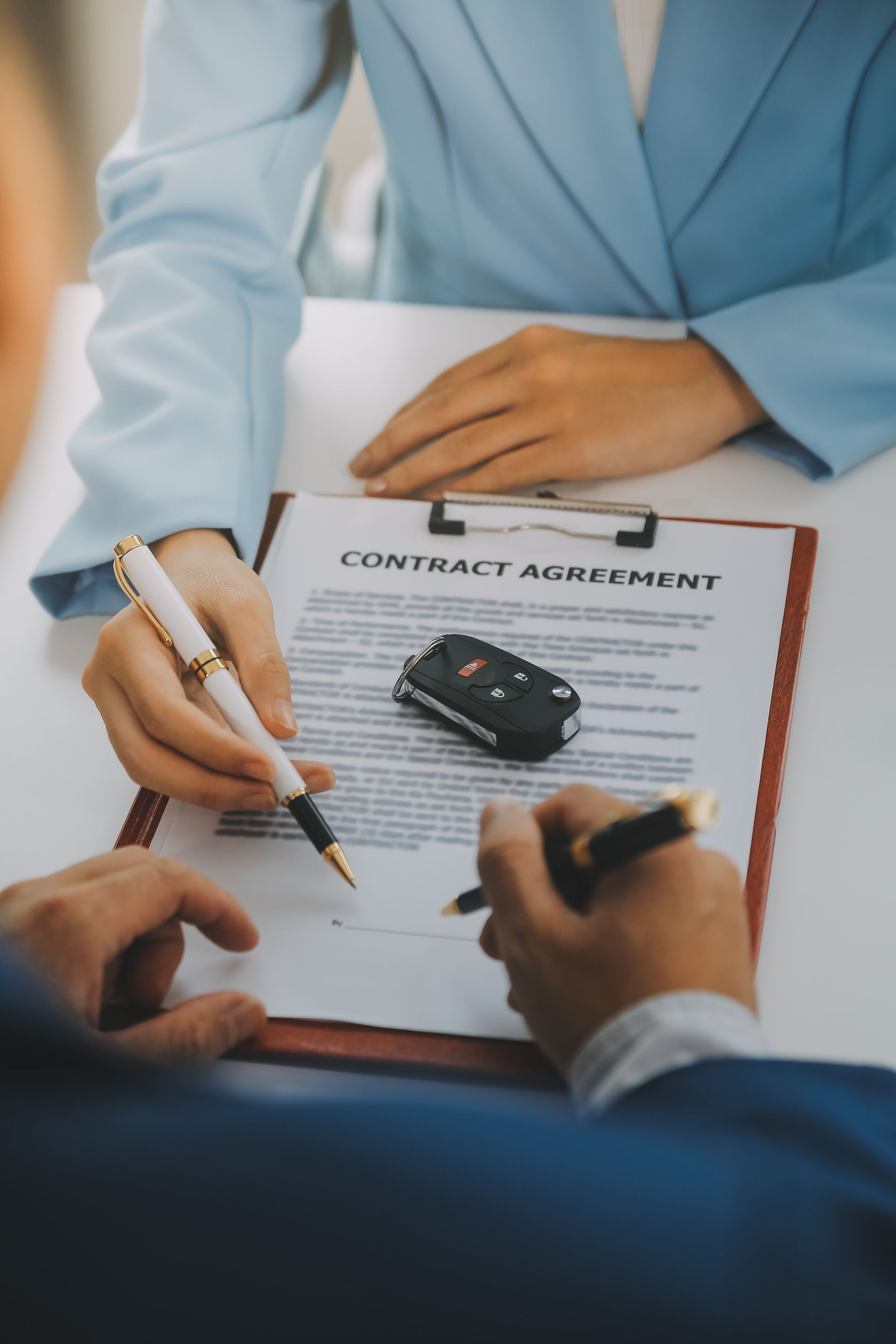 Two people in business attire sign a car contract agreement, with a car key fob