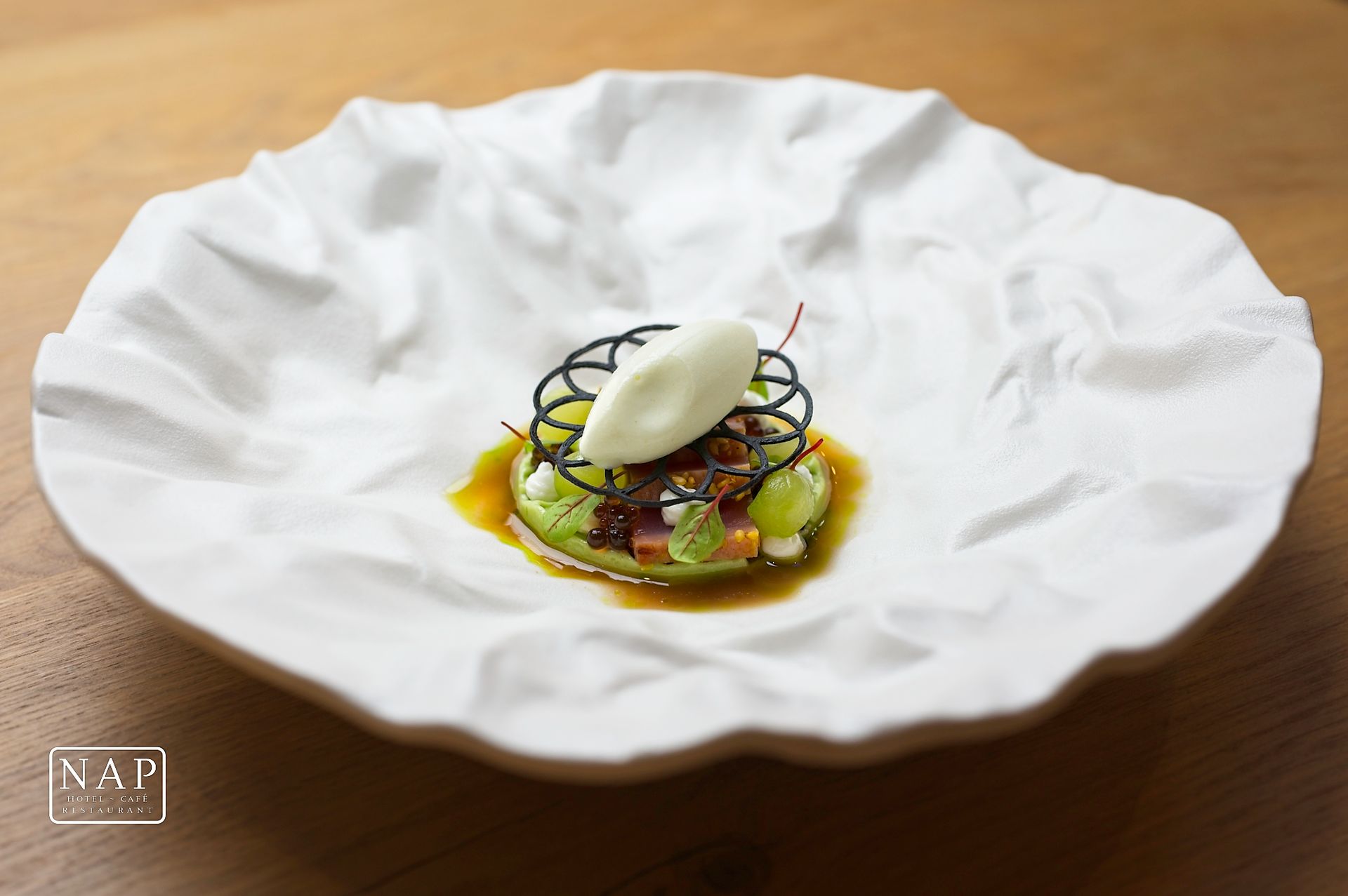 Plated gourmet dessert on a white scalloped dish with green garnish and a scoop of ice cream