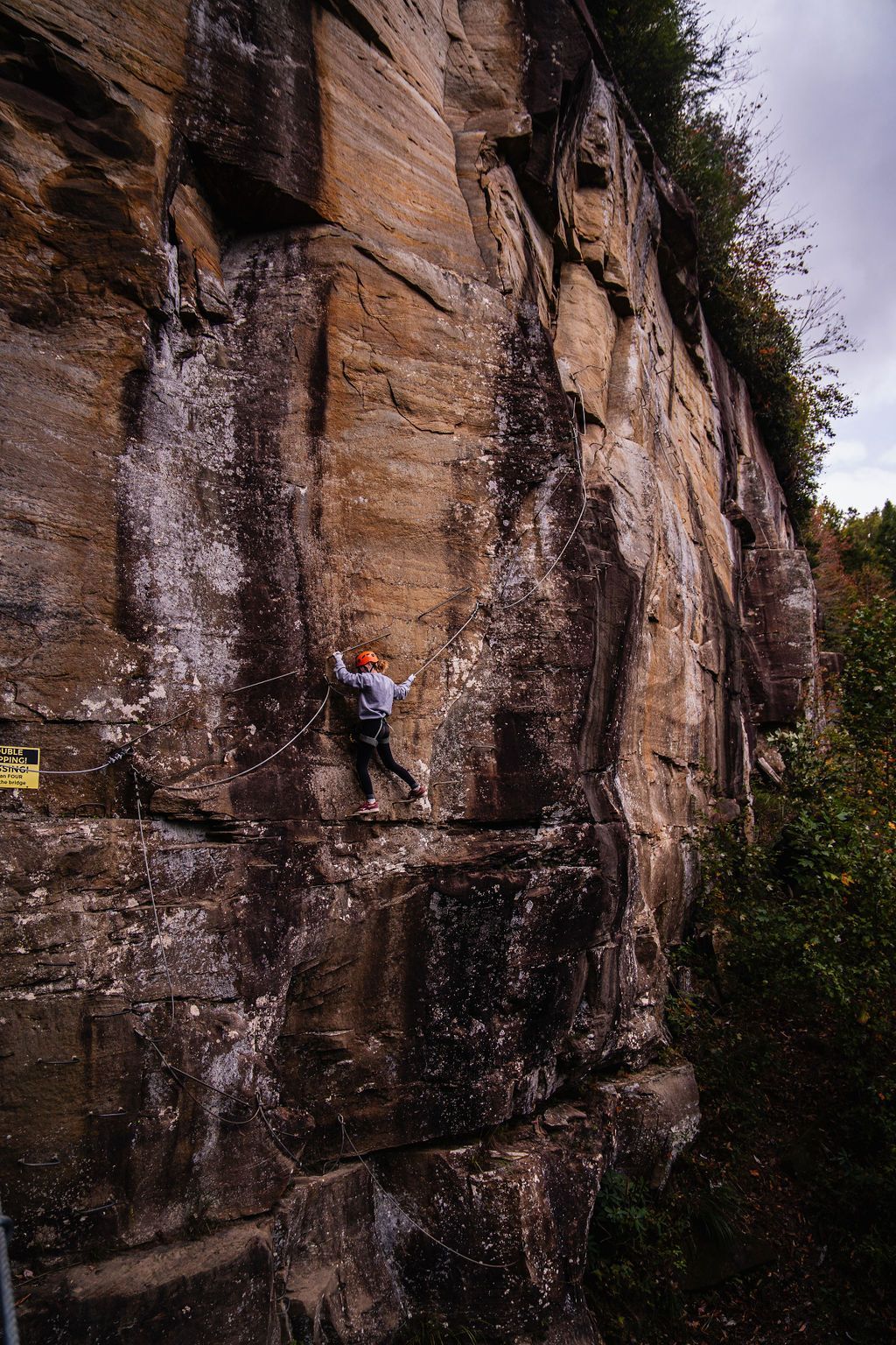 A woman climbs the steep terrain of the red river gorge via ferrata