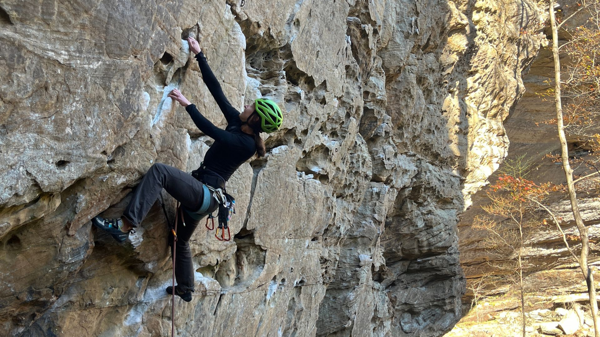 Climber in a helmet and harness on a Red River Gorge crag in autumn, near Rocktoberfest