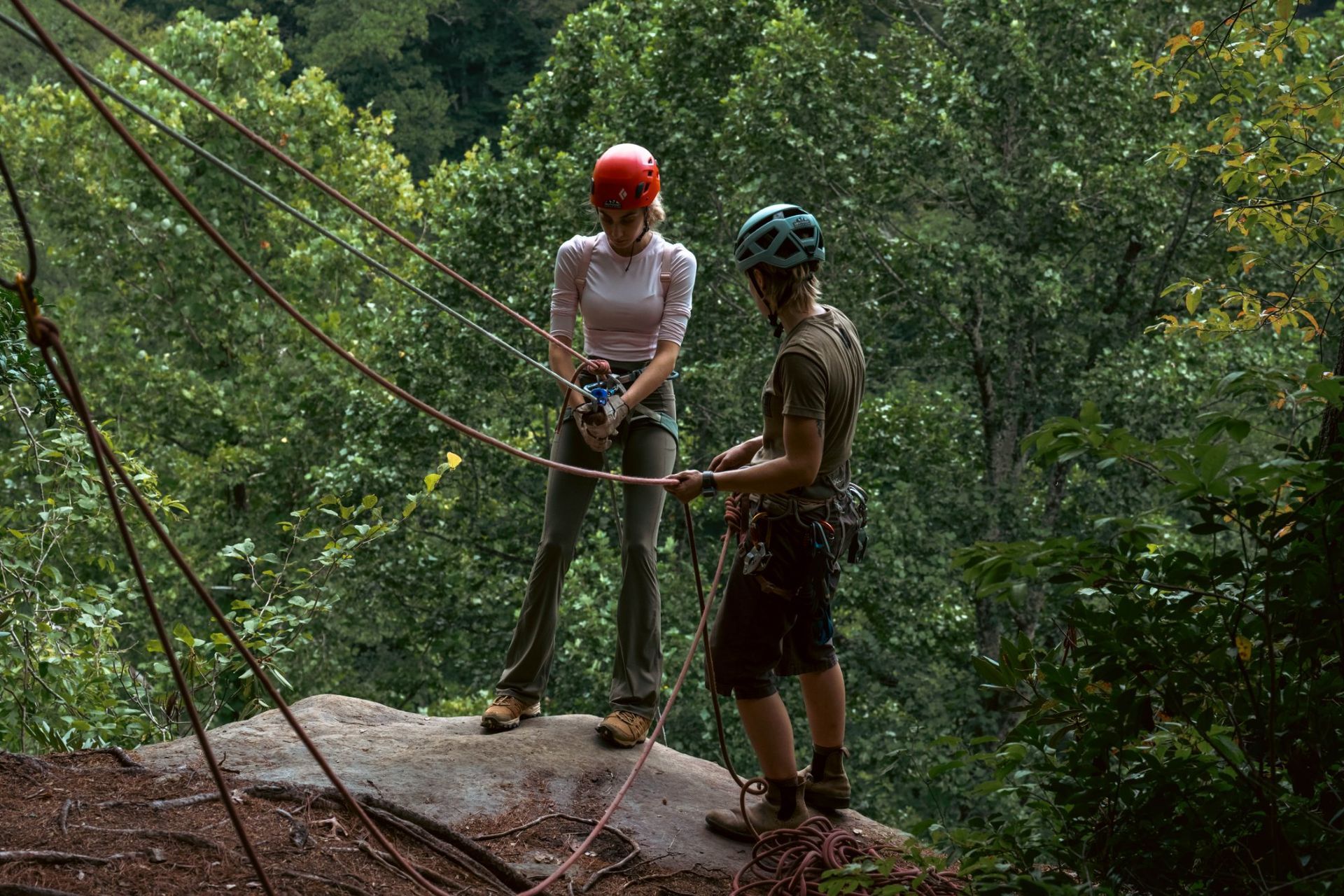 Guide coaching a rappeller on her rappel device at the top of a sandstone cliff during a guided rappelling trip in the Red River Gorge