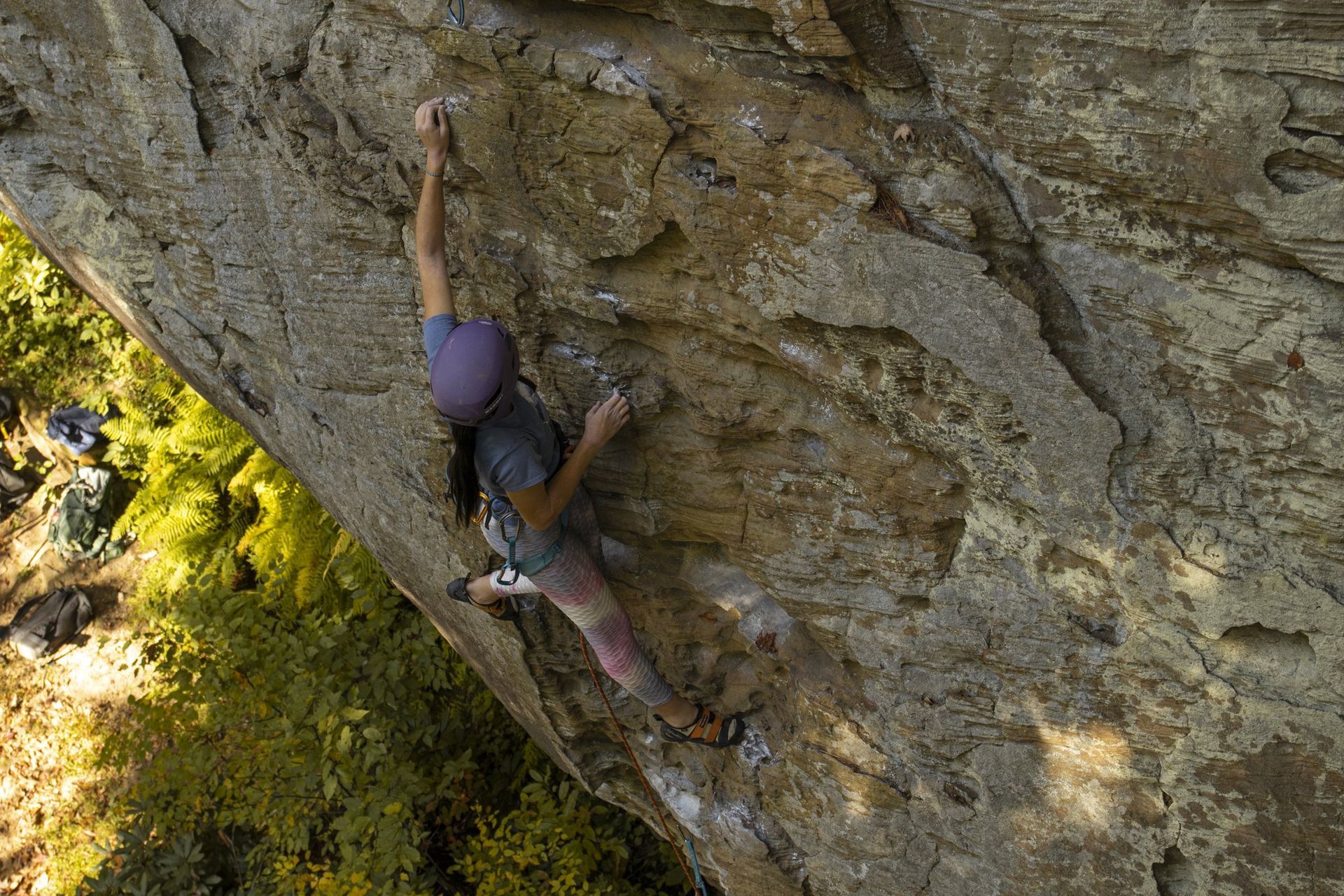 Climber in a purple helmet reaching for a hold on overhanging Red River Gorge sandstone