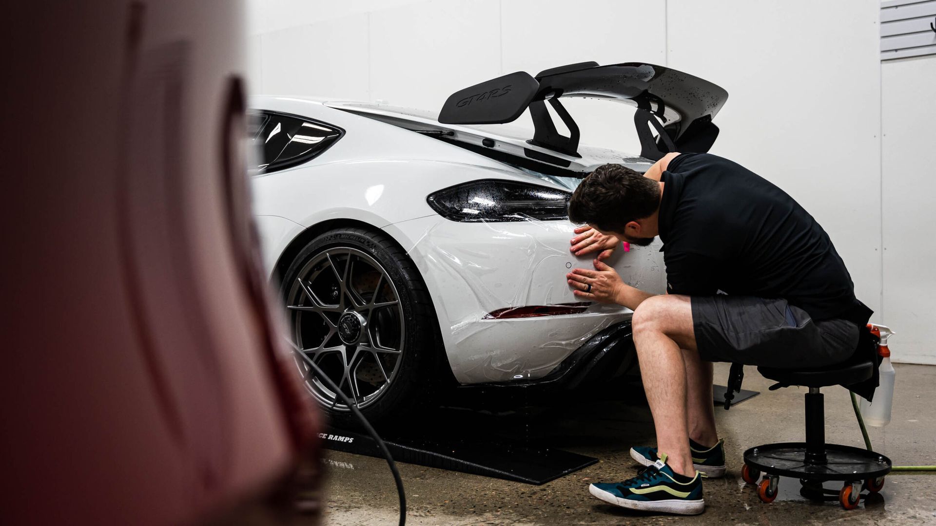 A man is sitting on a stool working on a white sports car.