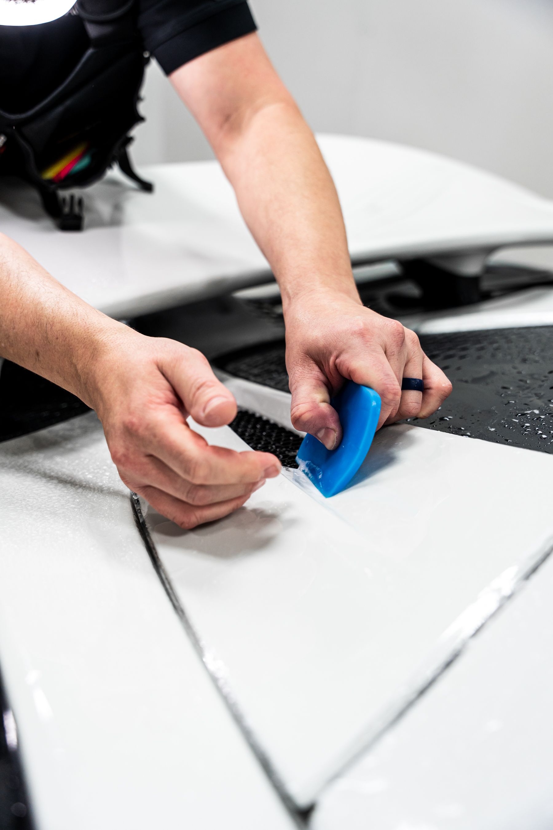 Person using a blue squeegee to apply film to a white car hood.