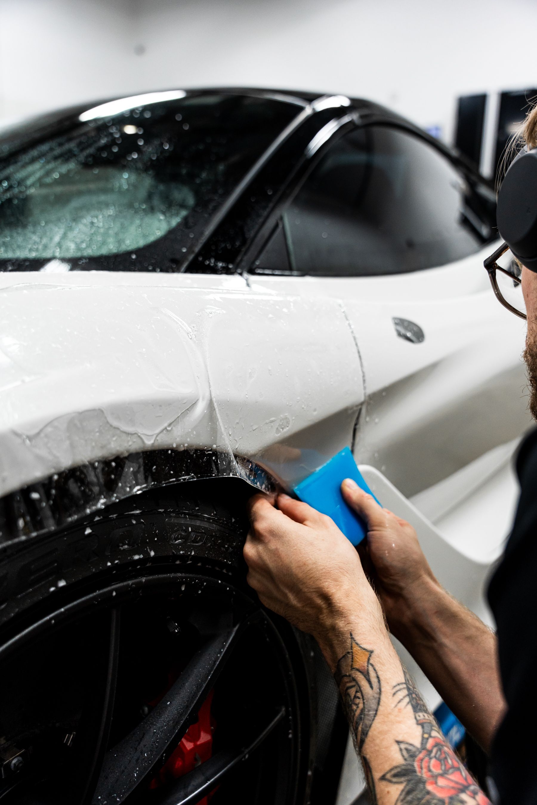 Man applying protective film to a white sports car. Blue tool in use.