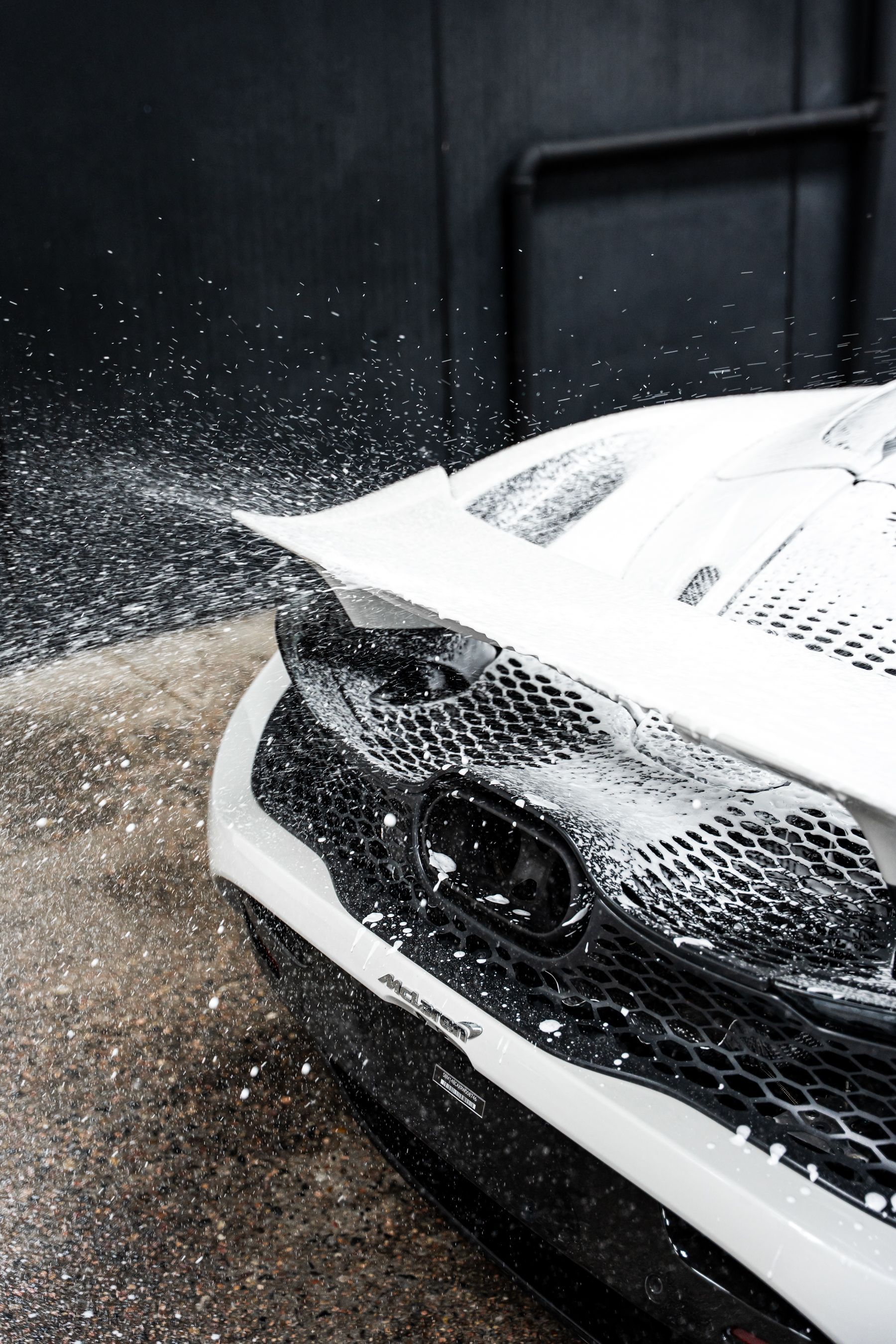White sports car covered in soapy foam, being washed in an industrial setting.