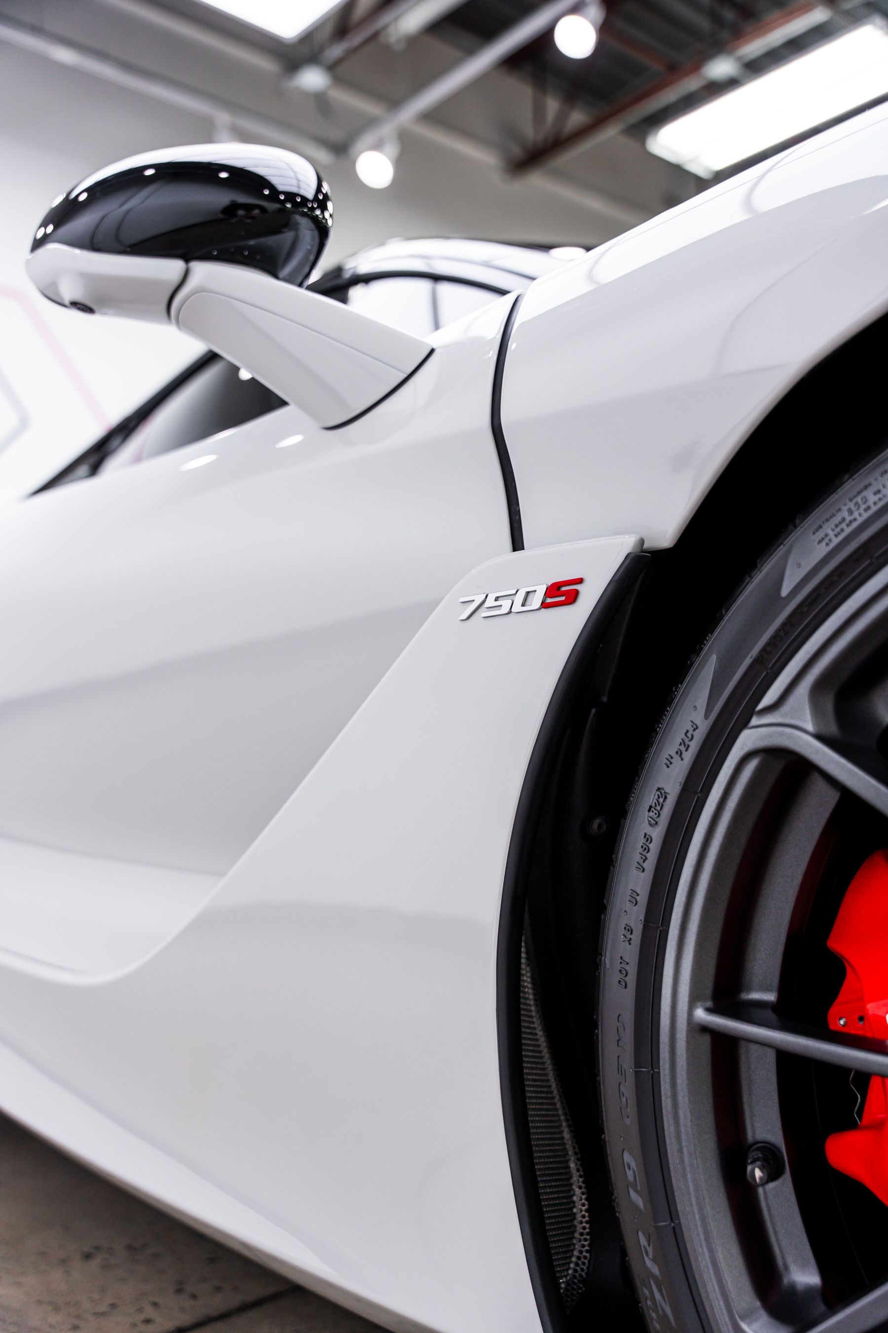 White McLaren 720S sports car with red brake calipers, side mirror, and 720S badge.