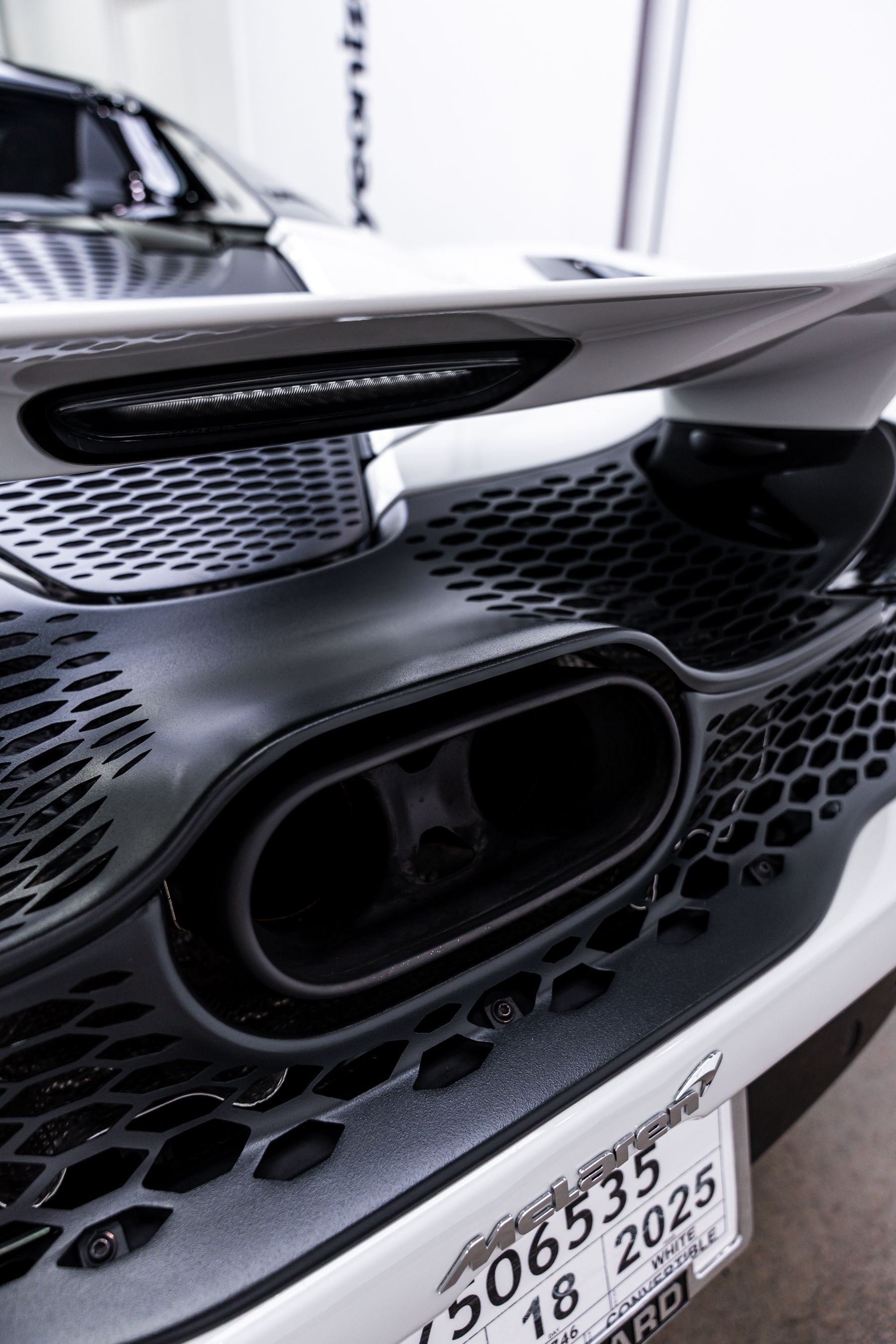 Close-up of a black exhaust pipe on a white sports car with a black honeycomb grill and spoiler.
