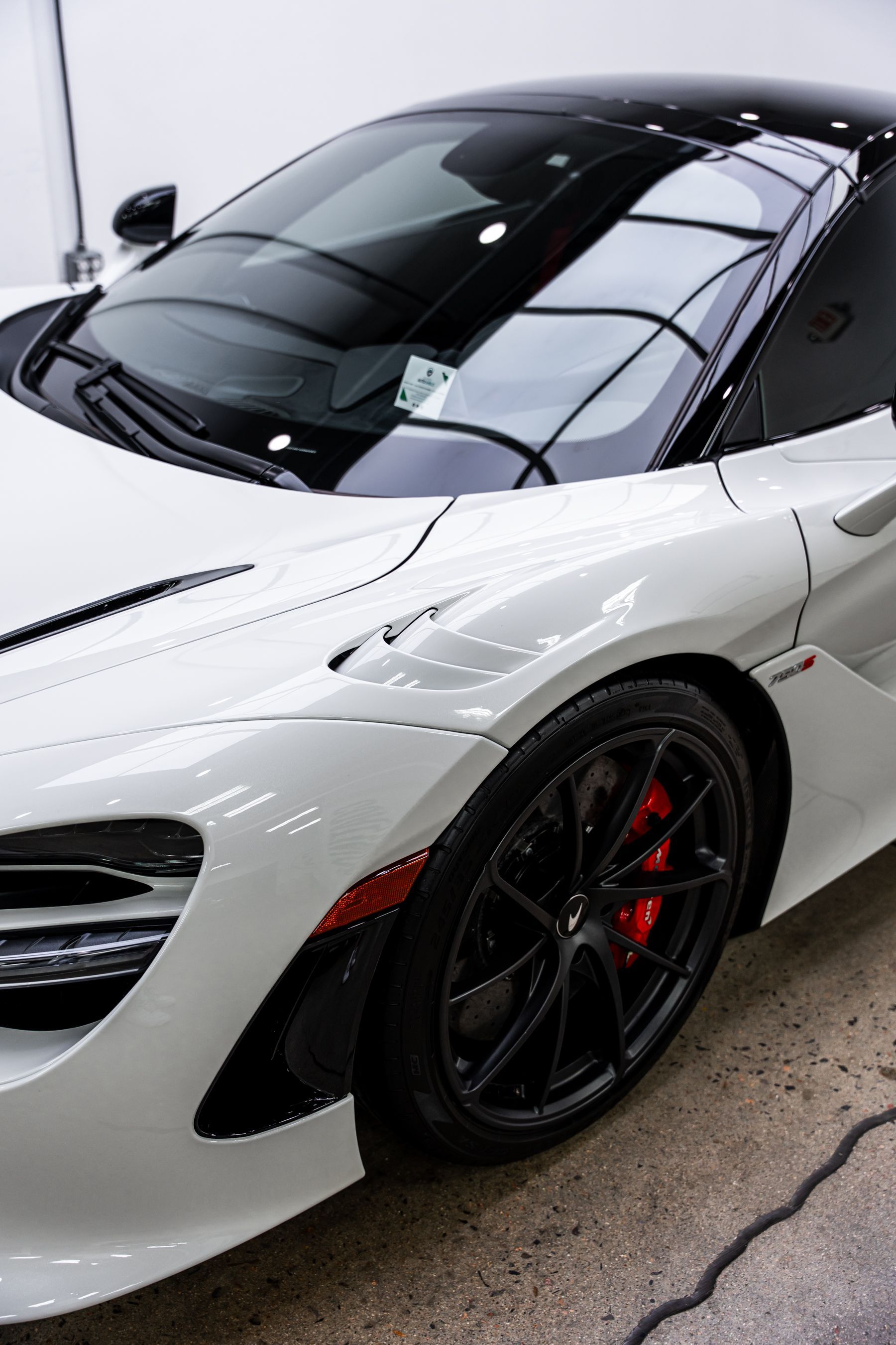 White McLaren sports car with black roof and wheels, red brake calipers.