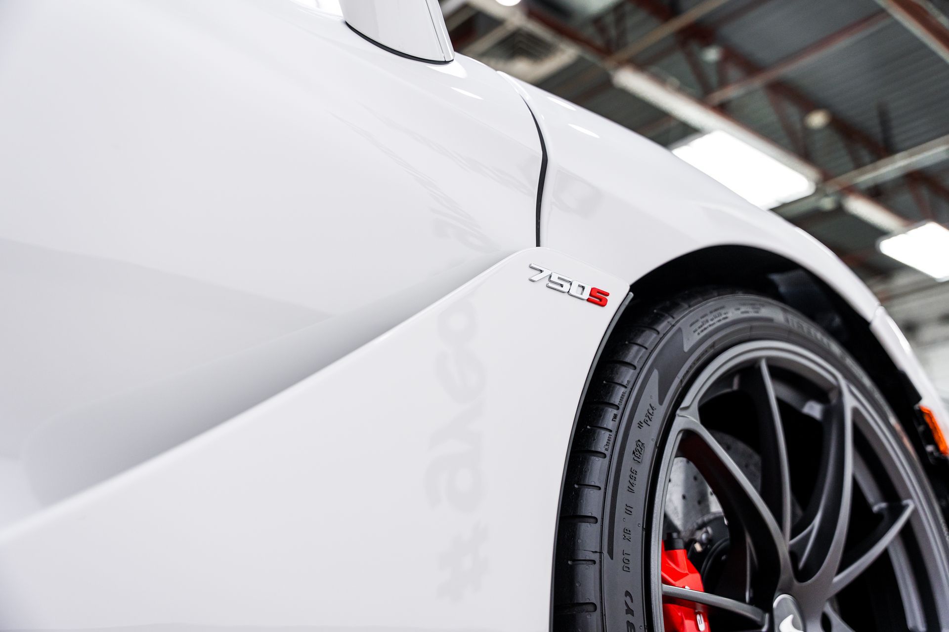 White McLaren 720S sports car, close up of front wheel and body panel, black rim, red brake caliper.
