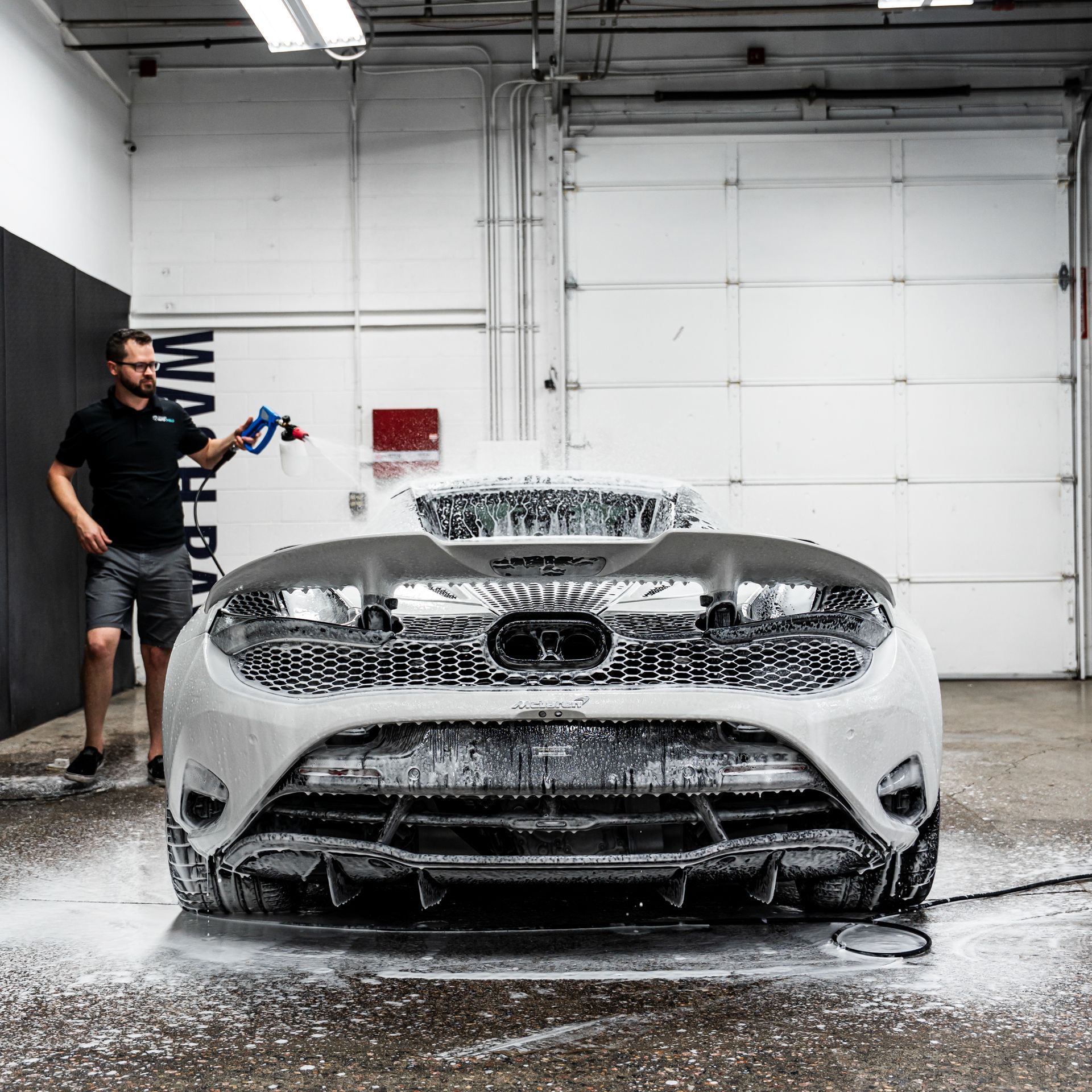 Man washing a white car with foamy soap in a garage.
