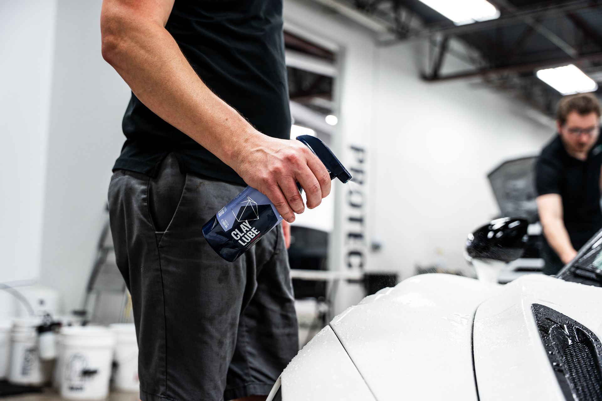 Man spraying a white car with a spray bottle in a garage.