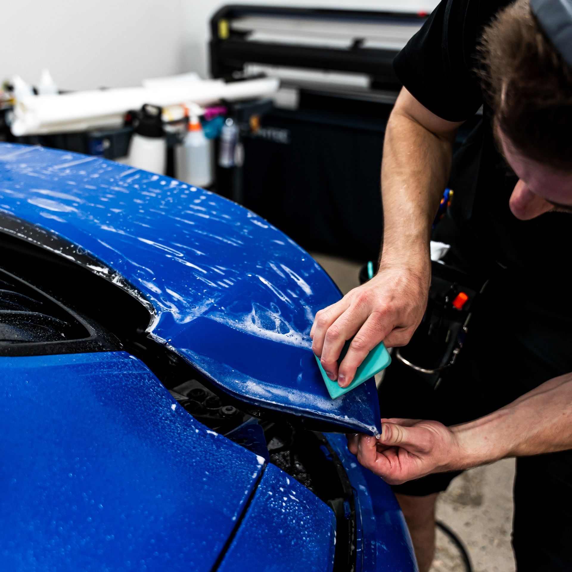 Person applying blue protective film to a blue car hood.